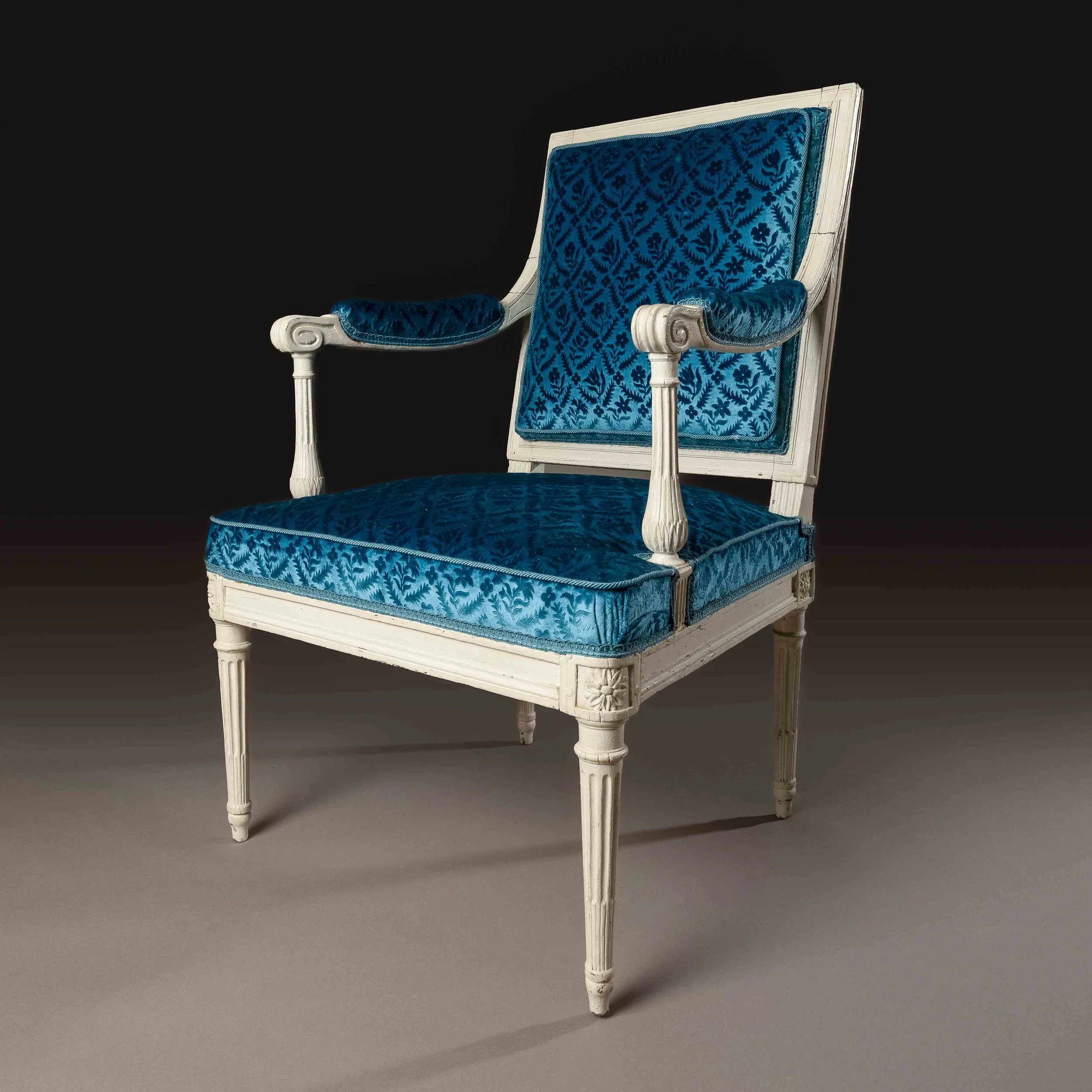 Chaise ancienne en bois blanc avec un tissu à motifs bleus et une assise rembourrée.