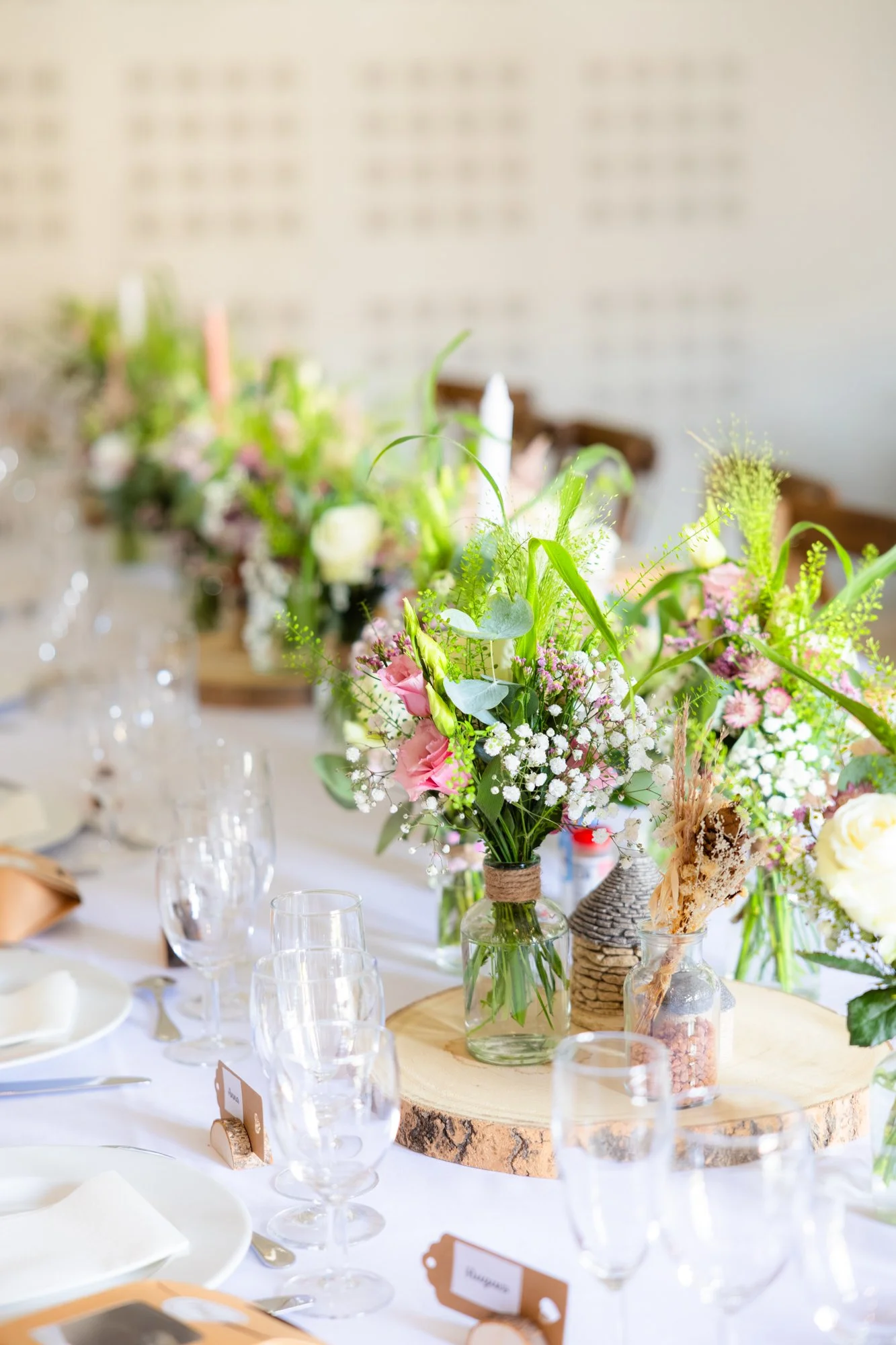 Vase de fleurs colorées en centre de table sur une table de réception ou de fête, avec des verres et assiettes autour, décorée et lumineuse.