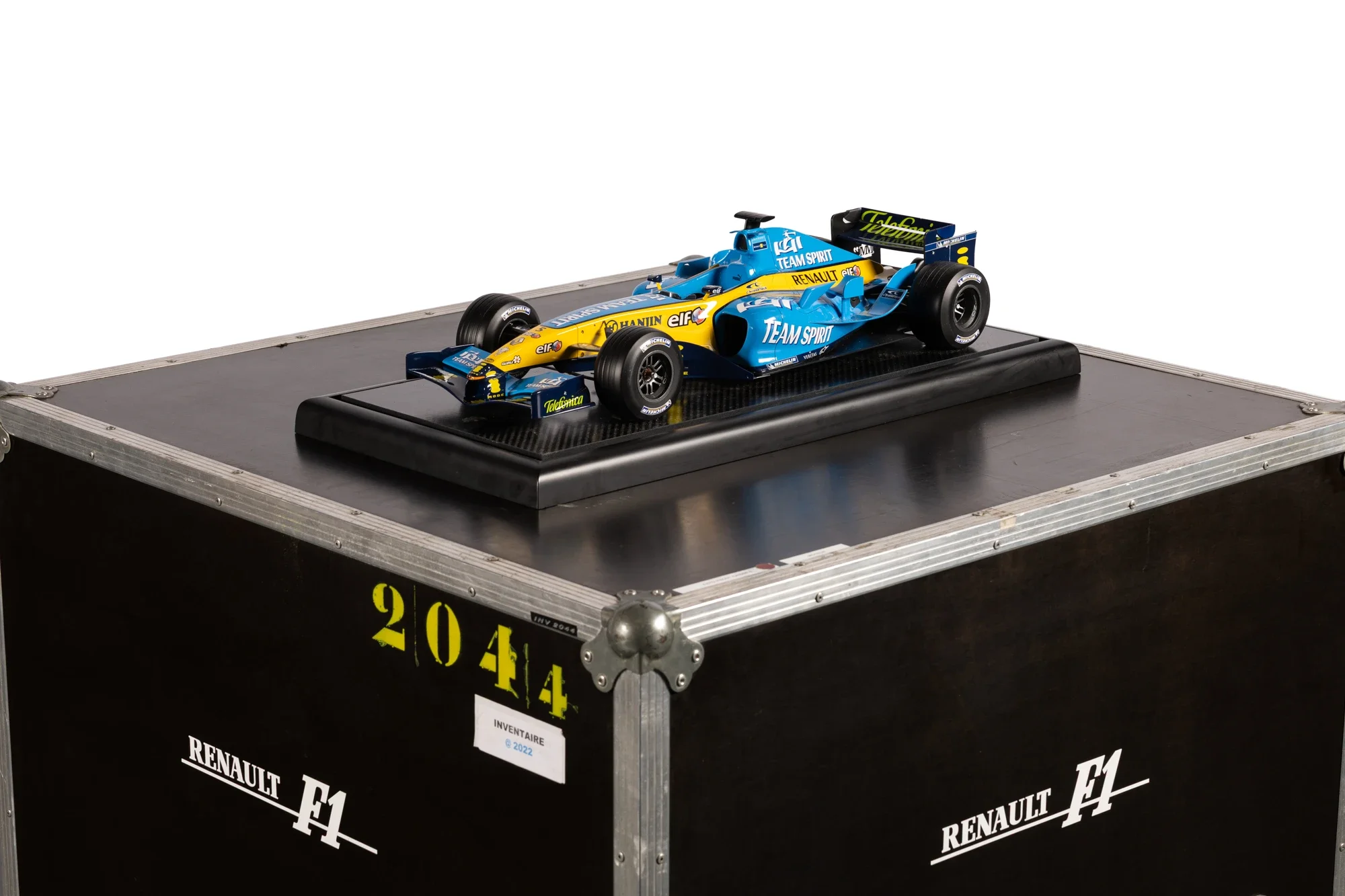 Une maquette de voiture de course de Formule 1 en bleu et jaune sur un socle noir avec étagère en métal. La voiture porte les logos de Renault, Team Spirit, Elf, et Telefunken.