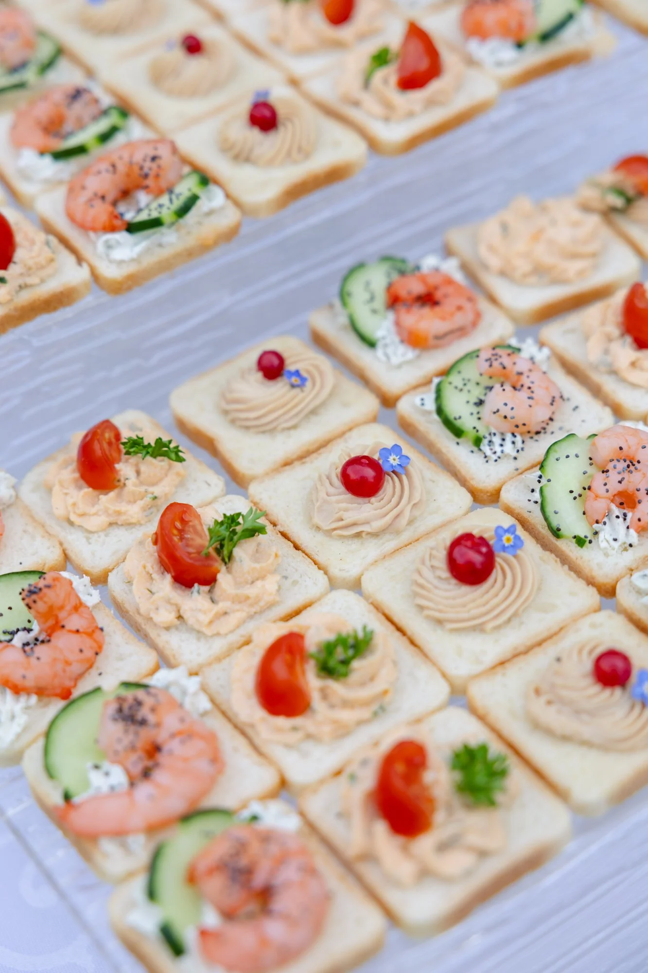 Vues rapprochées de plusieurs canapés variés avec garnitures telles que crevettes, tomate, concombre, fromage, et herbes, disposés sur une surface transparente.