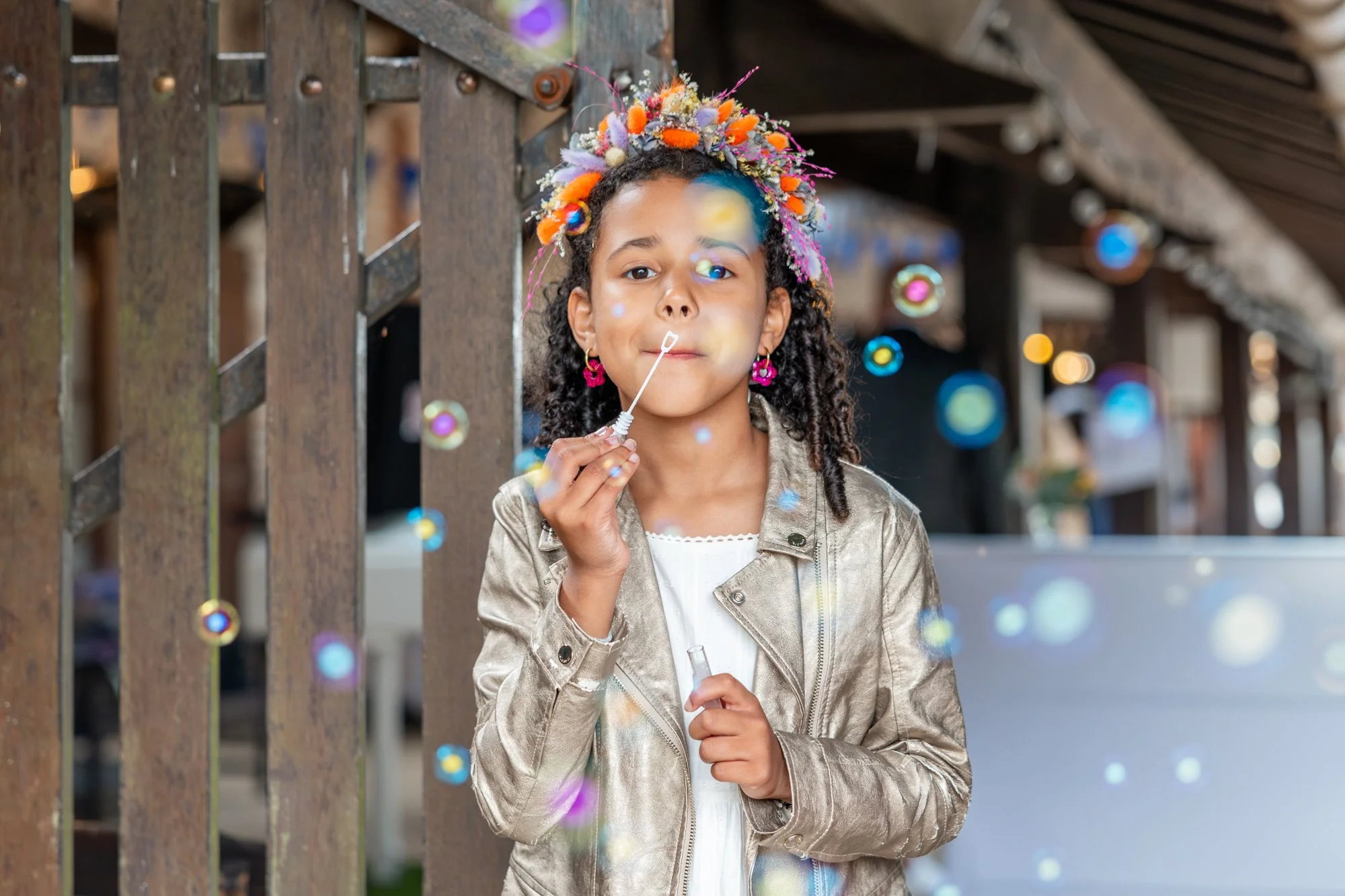 Une jeune fille avec un serre-tête de fleurs colorées, tenant un bulleur à bubble tea, en train de souffler des bulles de savon, sous un éclairage intérieur.