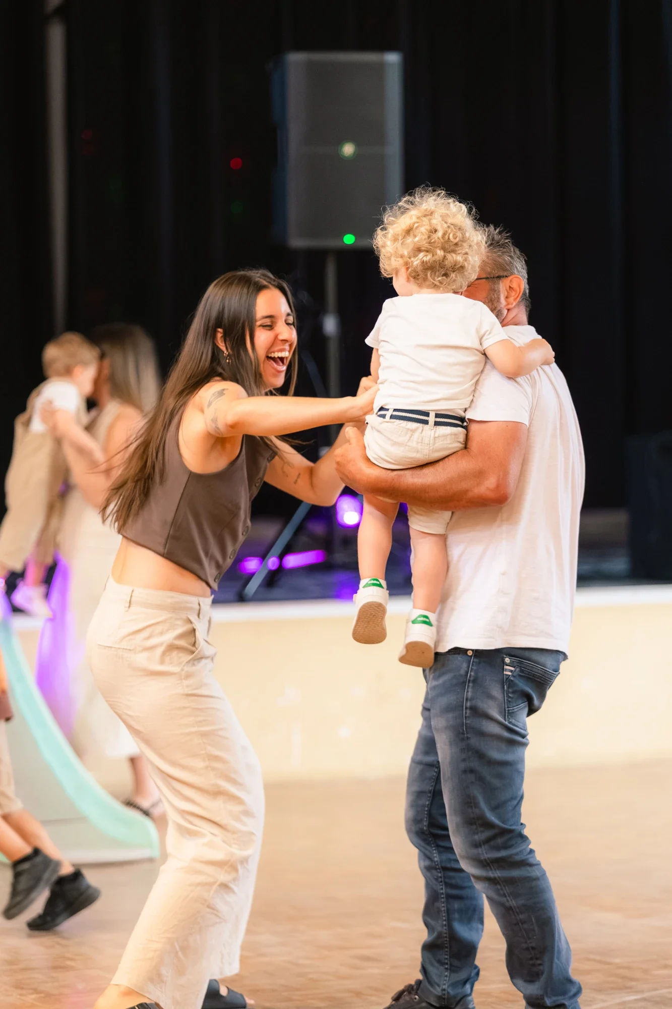 Une femme souriante danse avec un homme qui tient un enfant dans ses bras dans une salle de danse.