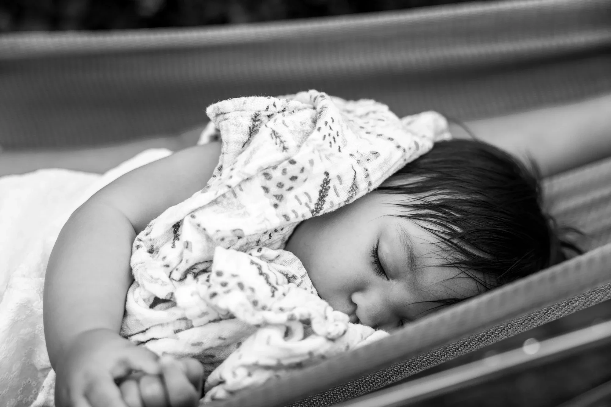 Une jeune enfant dort sur un lit, recouverte d'une couverture multicolore, avec ses yeux fermés et ses cheveux bruns. La photo est en noir et blanc.