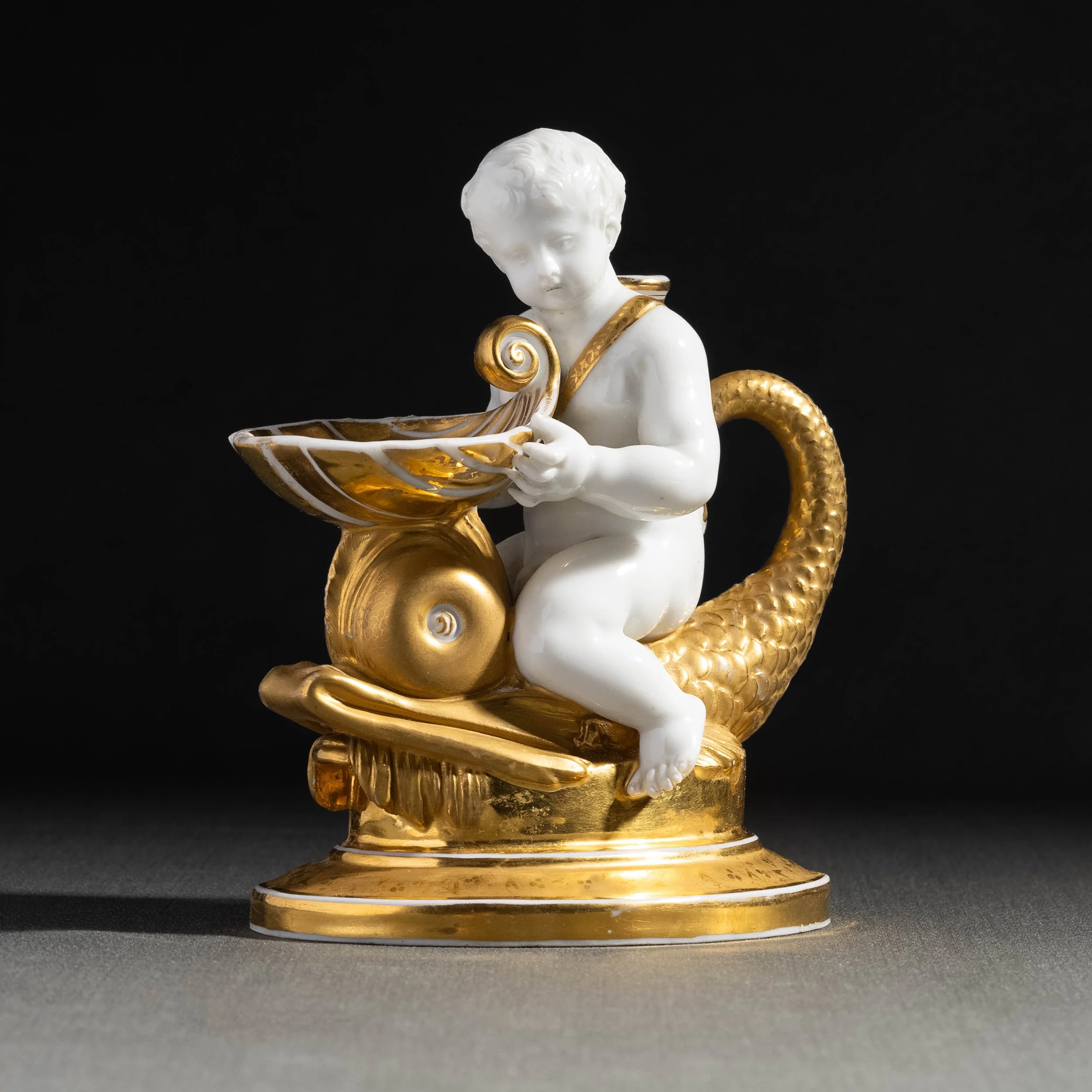 Statue de petit garçon en porcelaine blanc avec des accents dorés, tenant un bol, avec une queue de dragon dorée, sur un socle en or.