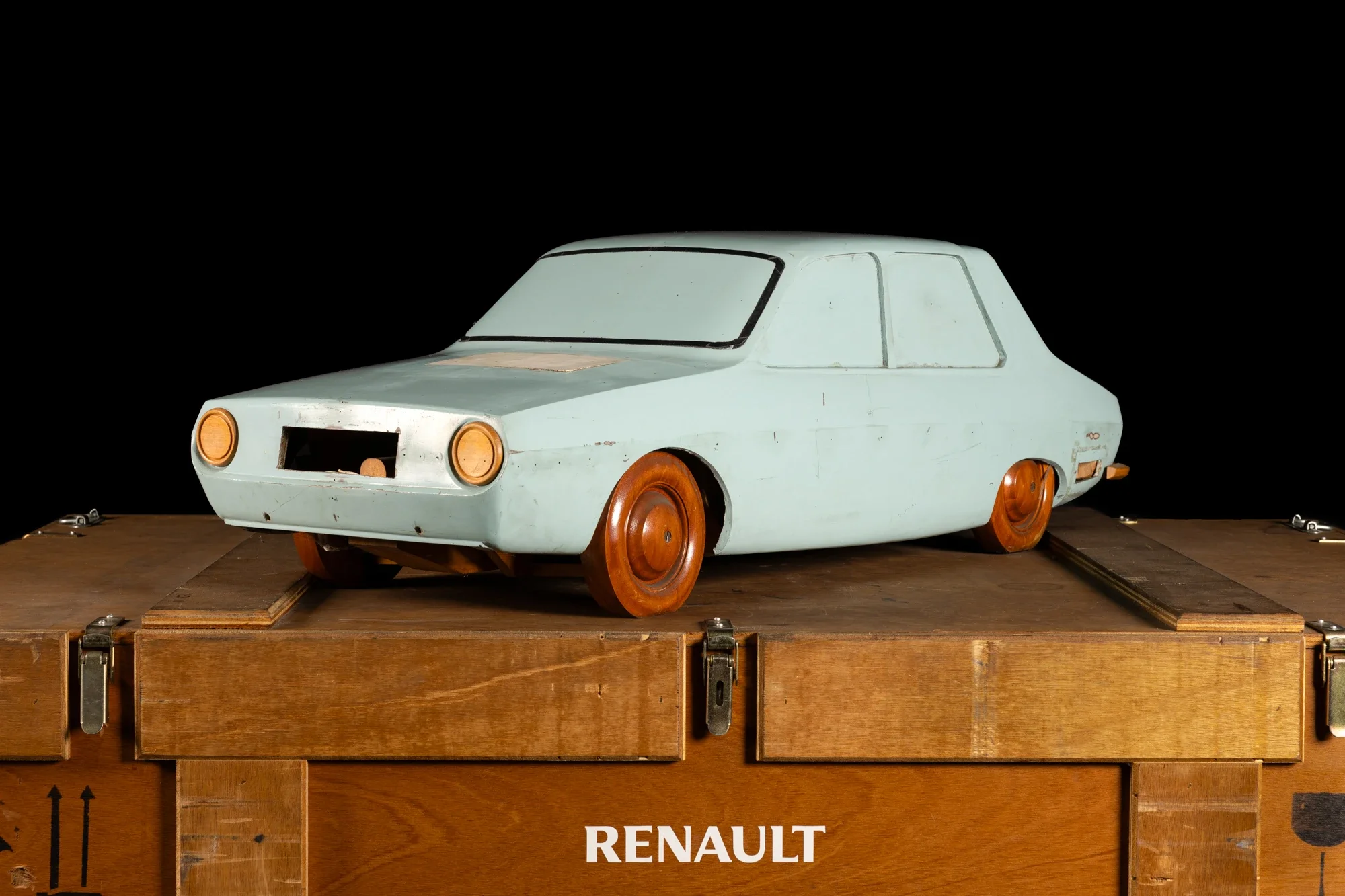 Modèle réduit d'une voiture Renault ancienne sur une plateforme en bois, fond noir.