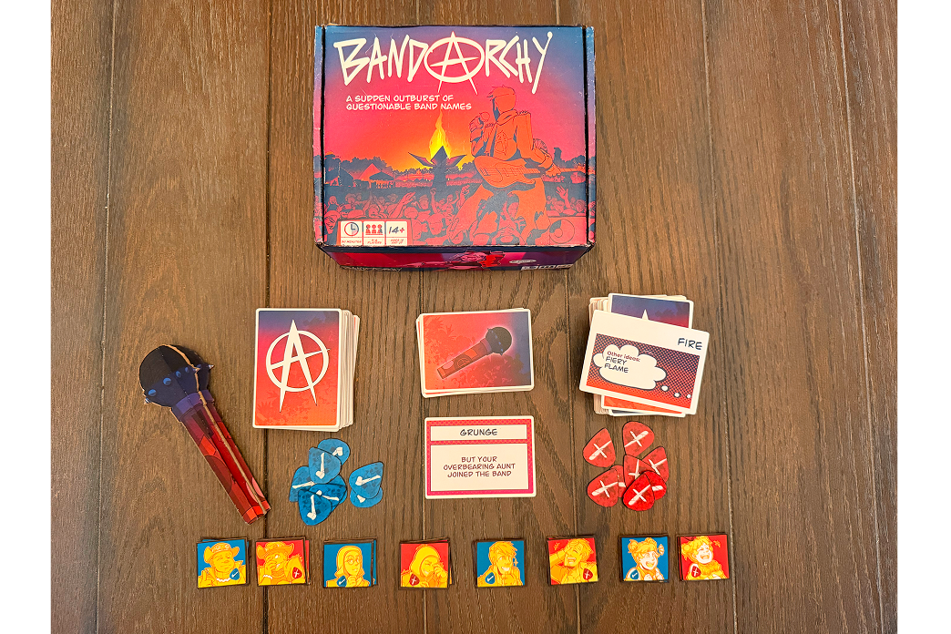 The game box with all of its contents laid on the table. 16 character tiles, 216 word cards, 40 genre cards, 16 guitar picks, faux microphone