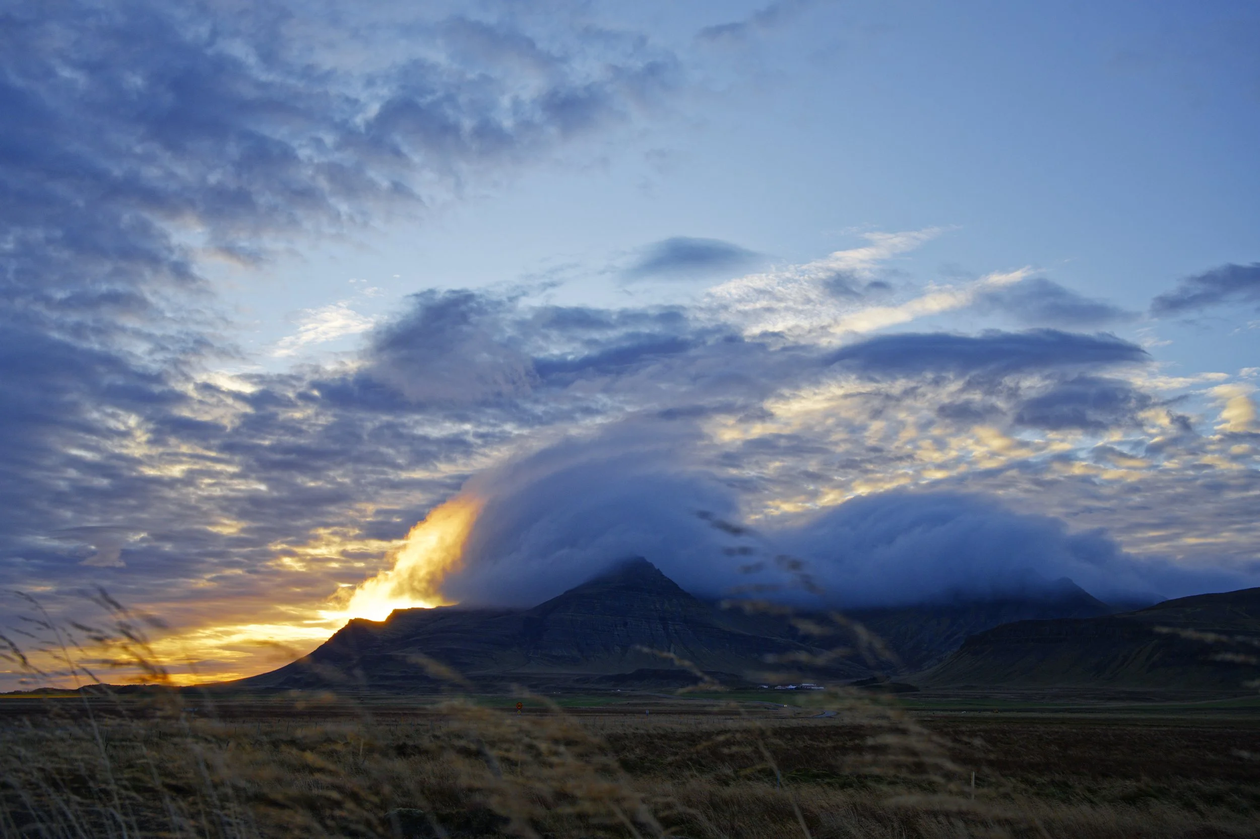 Sunset behind mountains with clouds in the sky.