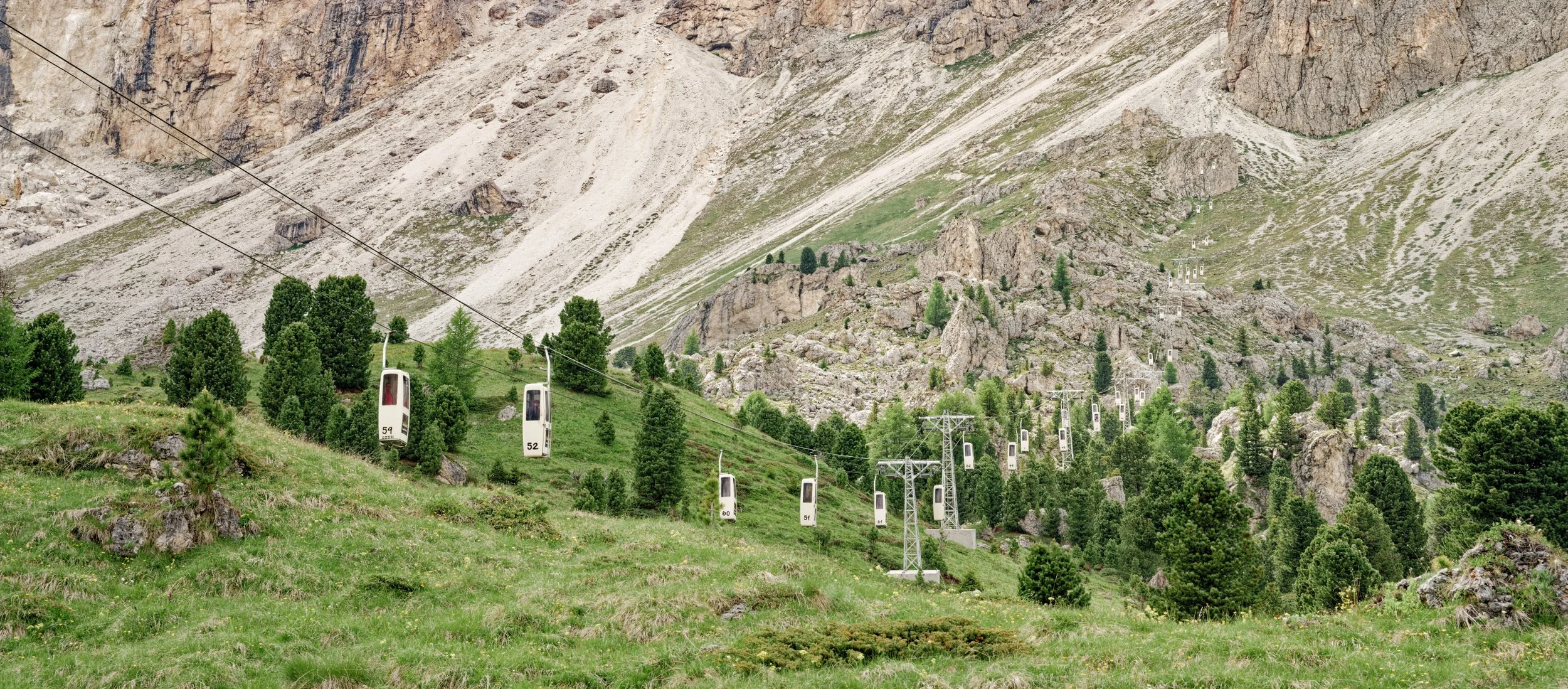 Cable cars ascending a green hillside with trees, rocks, and a mountain in the background.