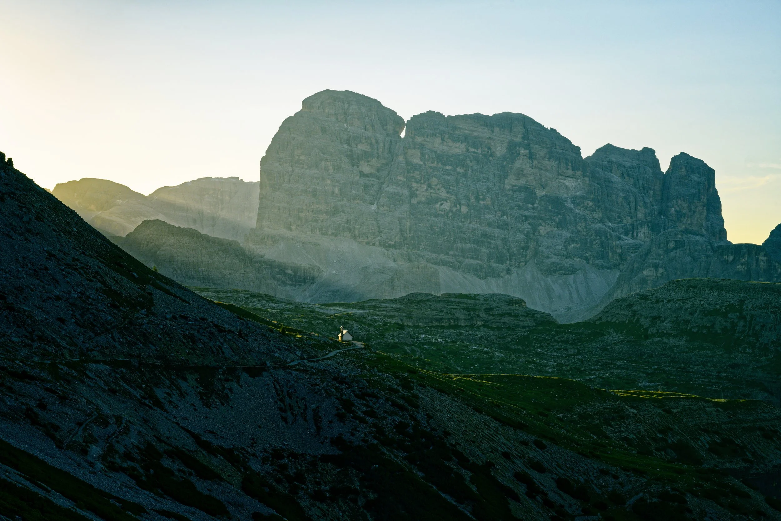 Mountain landscape during sunset with rocky slopes in the foreground and towering cliffs in the background.