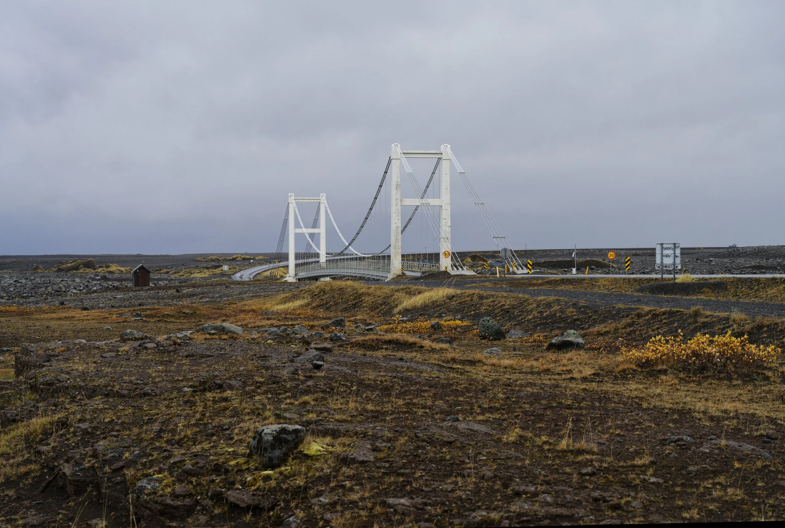 A suspension bridge crossing a rocky, barren landscape under a cloudy sky.