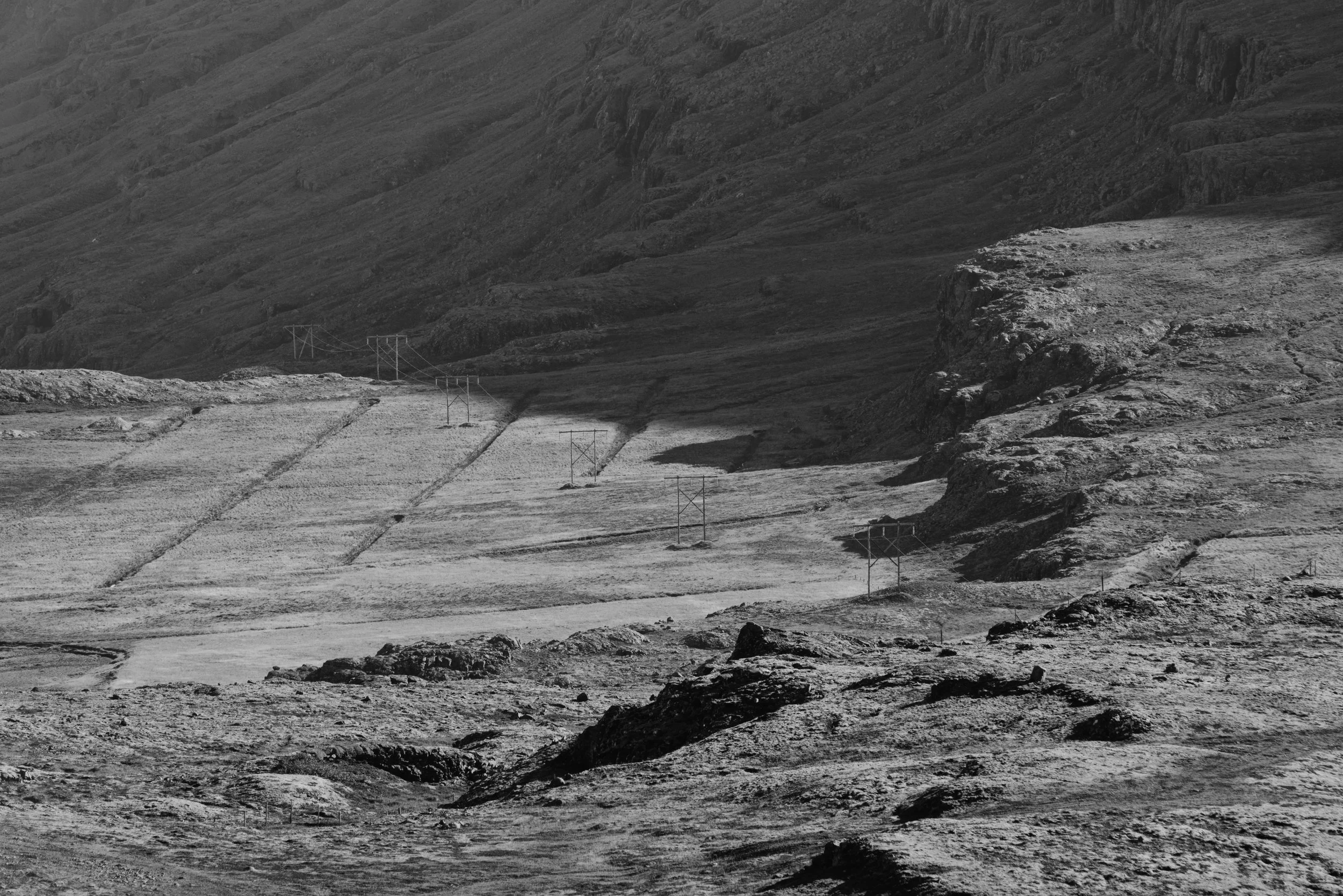 A black and white landscape photo of a mountainous area with power lines running through the terrain.