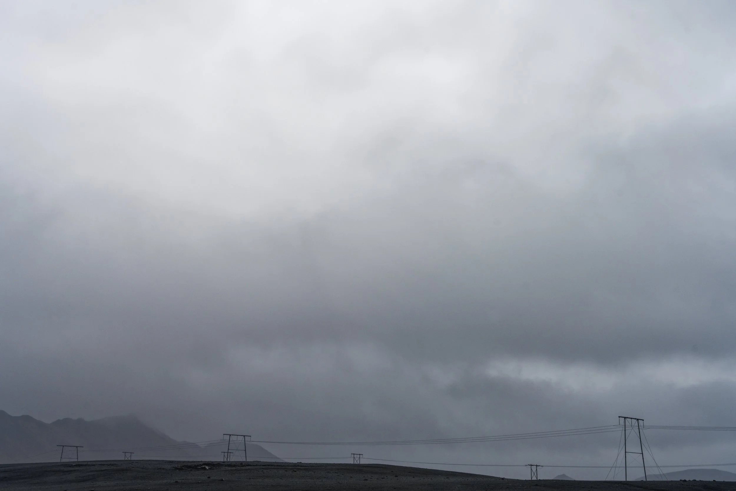 Overcast sky with high-voltage power lines and mountains in the distance.