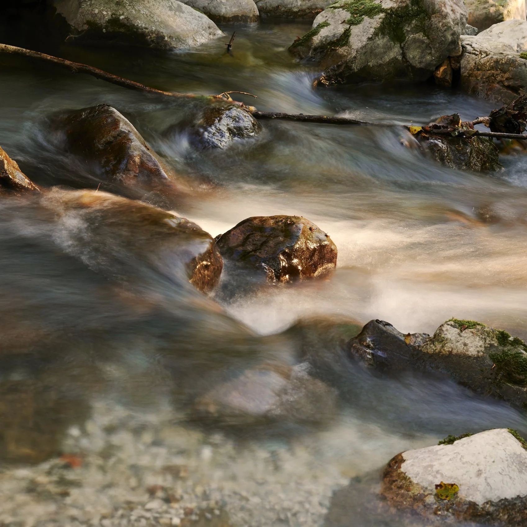 A flowing stream with rocks and moss along its banks, captured in a natural outdoor setting.