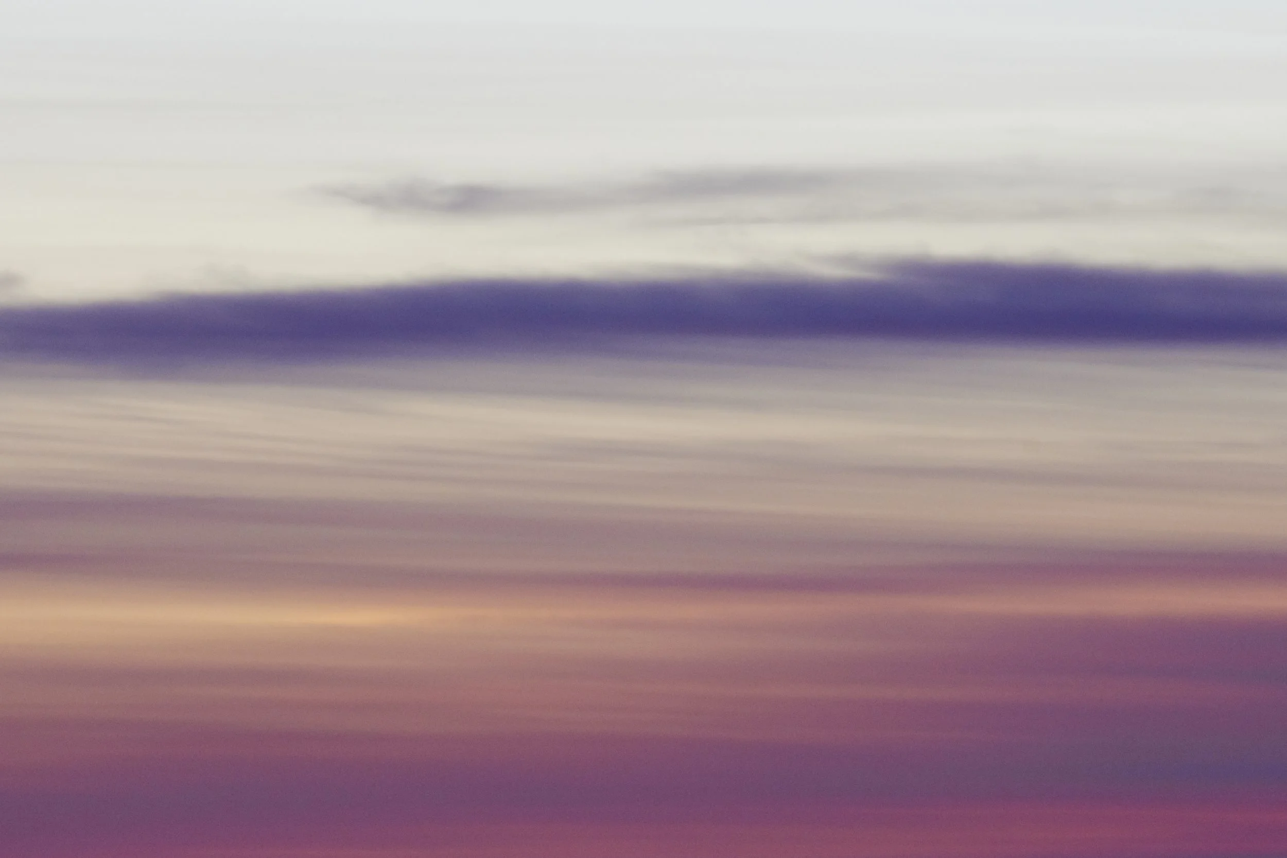 A colorful sky at sunset with horizontal bands of purple, pink, and beige clouds.