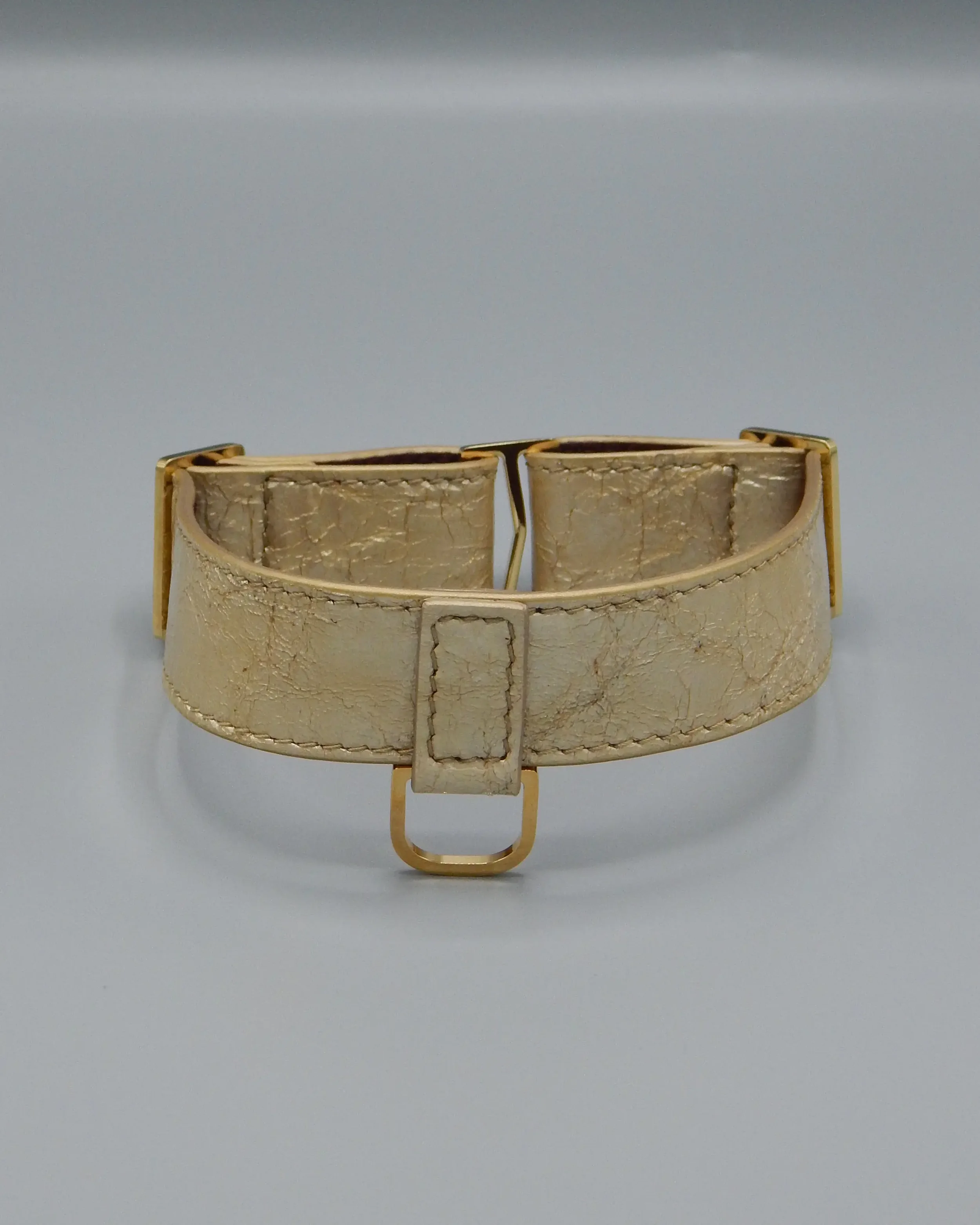 Bracciale in pelle beige con dettagli in metallo dorato, visto frontalmente su sfondo grigio.