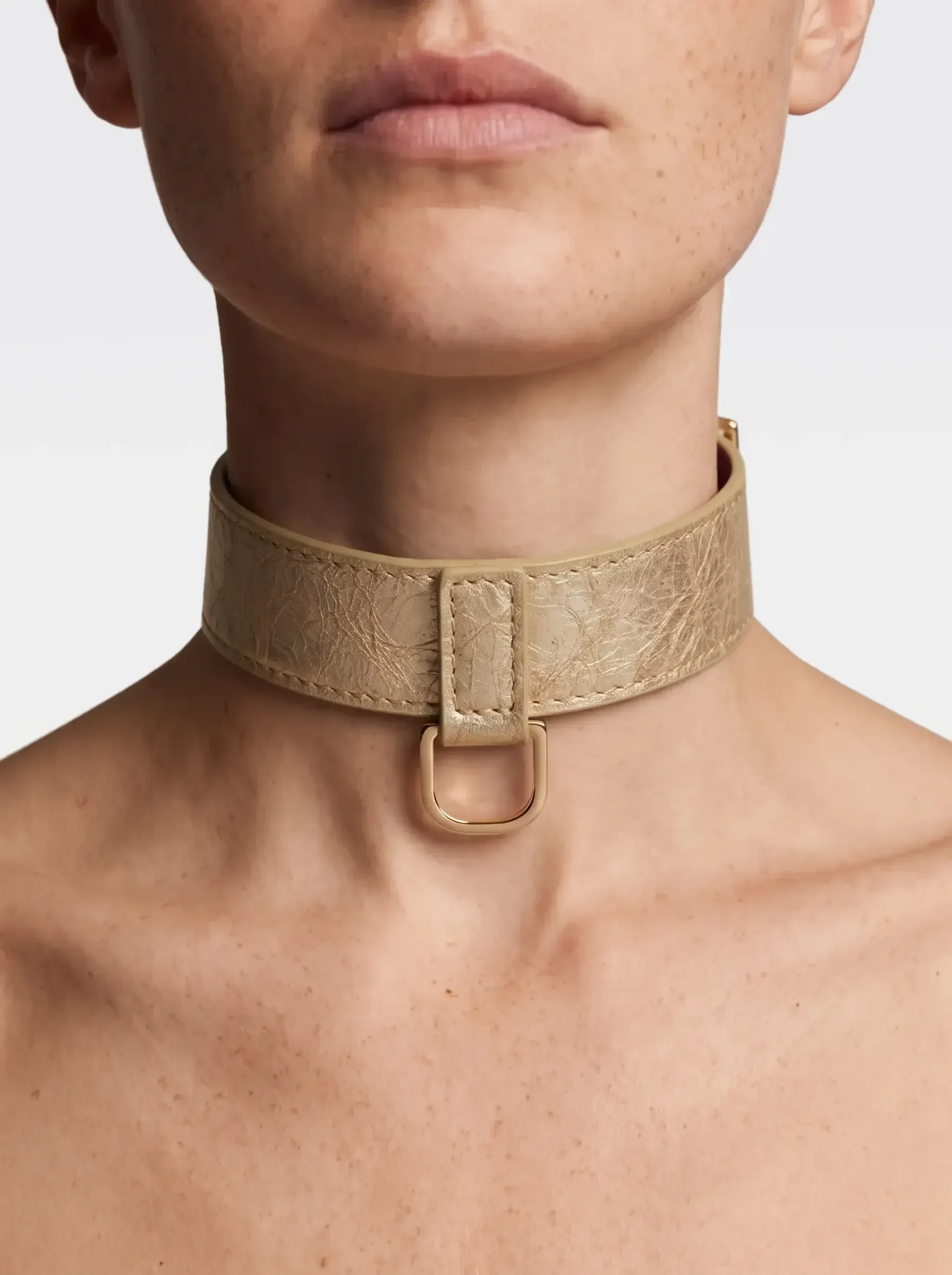 Dettaglio di una donna con pelle liscia e senza trucco che indossa una collana di pelle beige con una fibbia dorata.