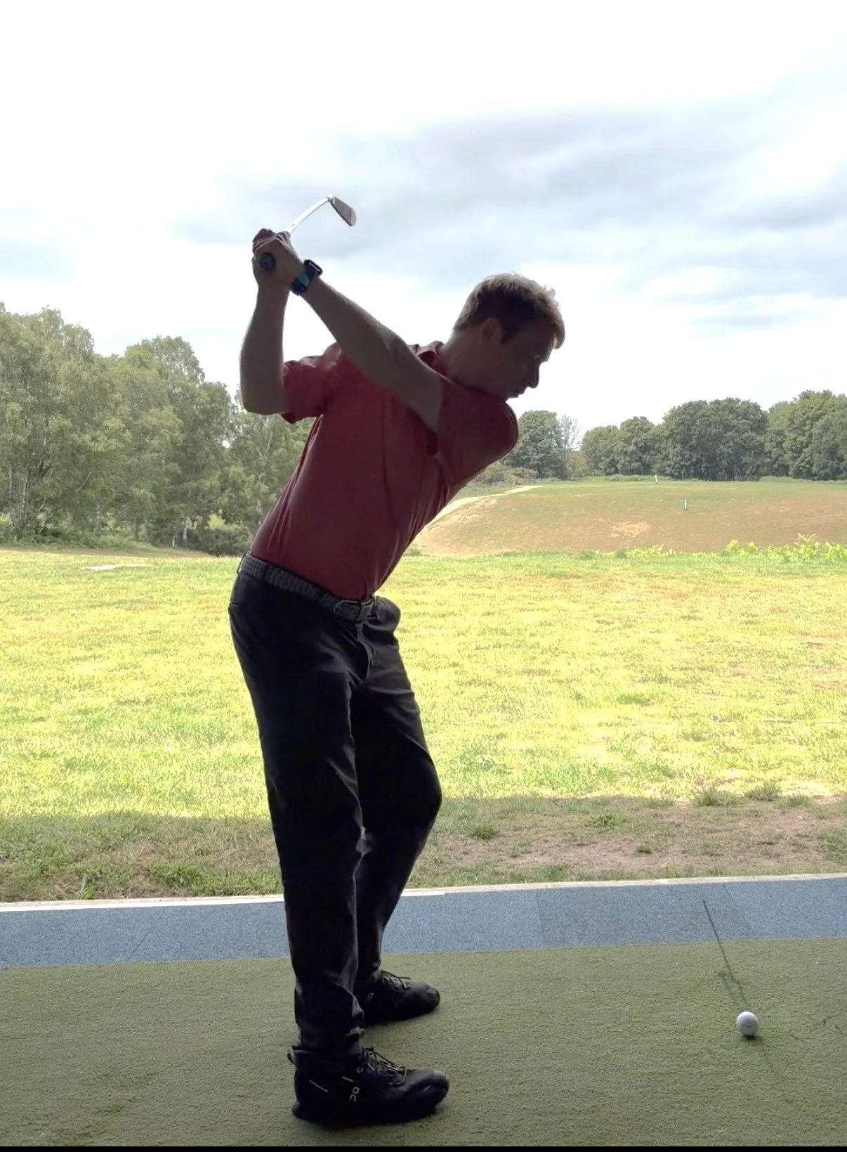 A man in a red shirt and black pants taking a golf swing in the studio at Woodbridge Golf Club in Suffolk.