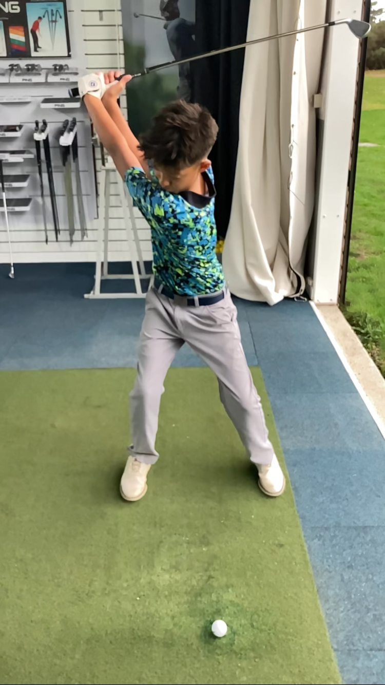 Young boy practicing golf indoors, preparing to hit a golf ball on a small mat in the swing studio at Woodbridge Golf Club in Suffolk