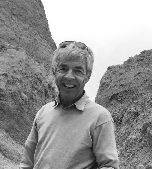 Smiling man with sunglasses on his head, standing between two large rock formations in a desert area.
