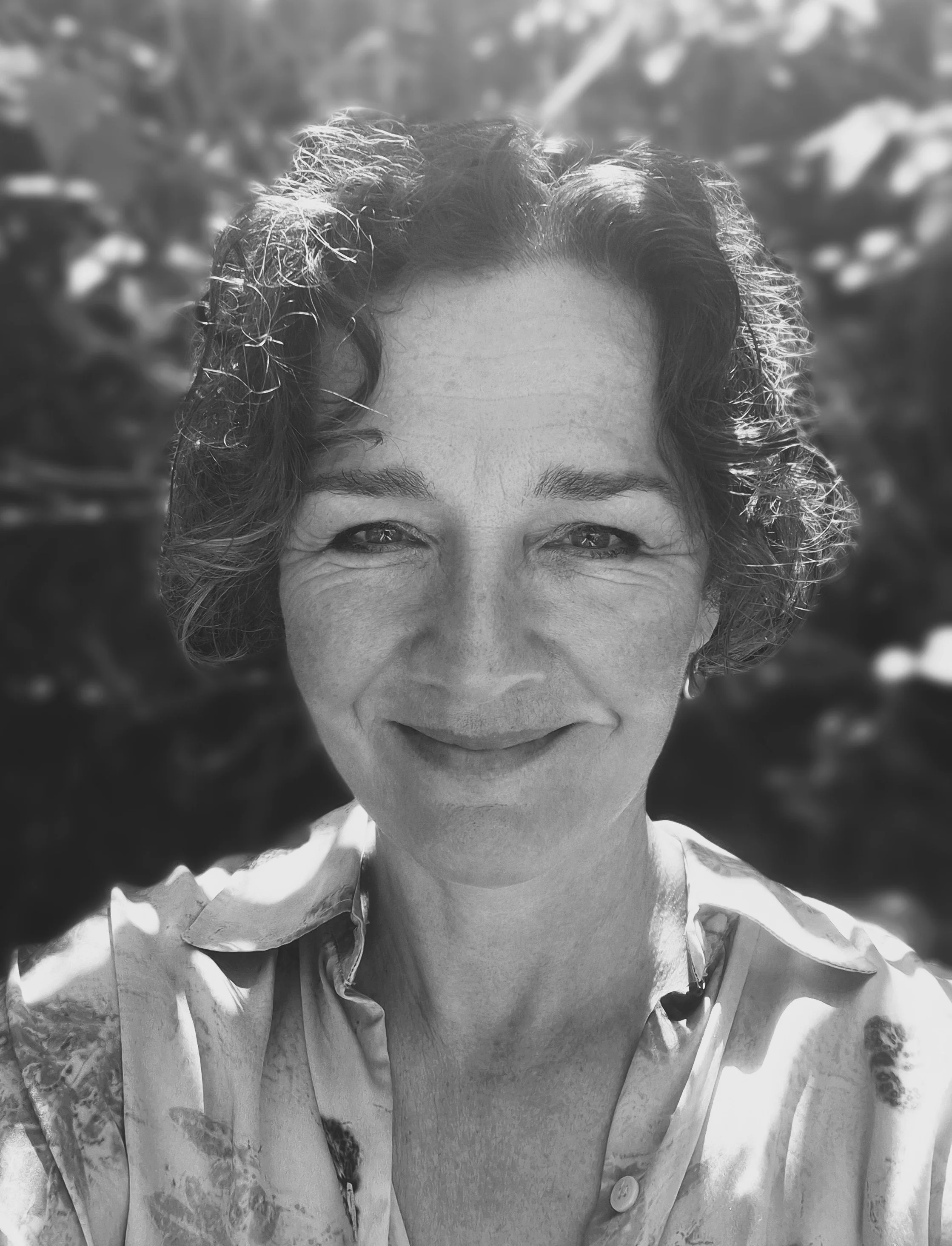 A smiling woman with curly hair in a close-up outdoor portrait, black and white photograph.