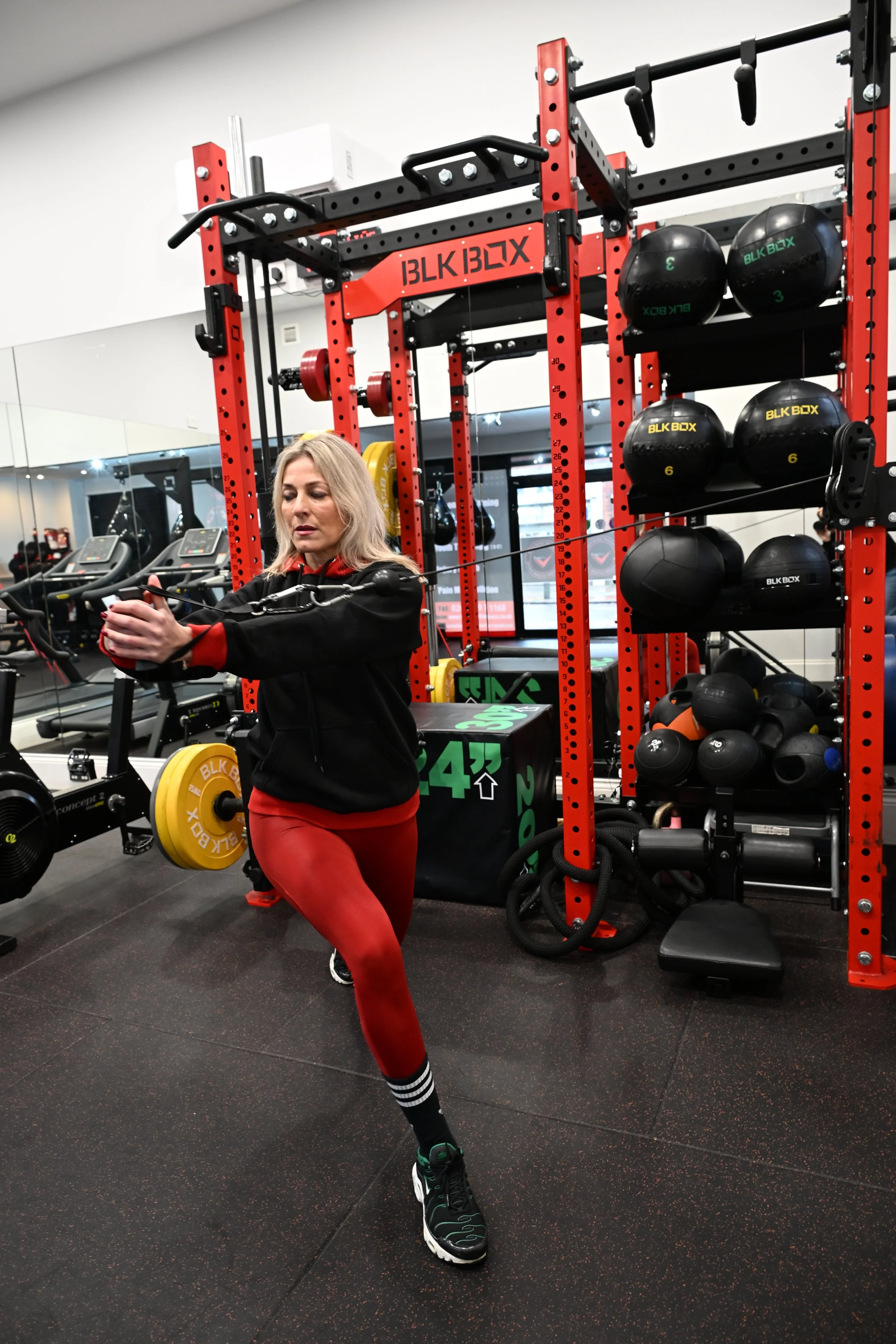 Personal trainer, Joan, using a cable machine at a gym, surrounded by fitness equipment and weights.