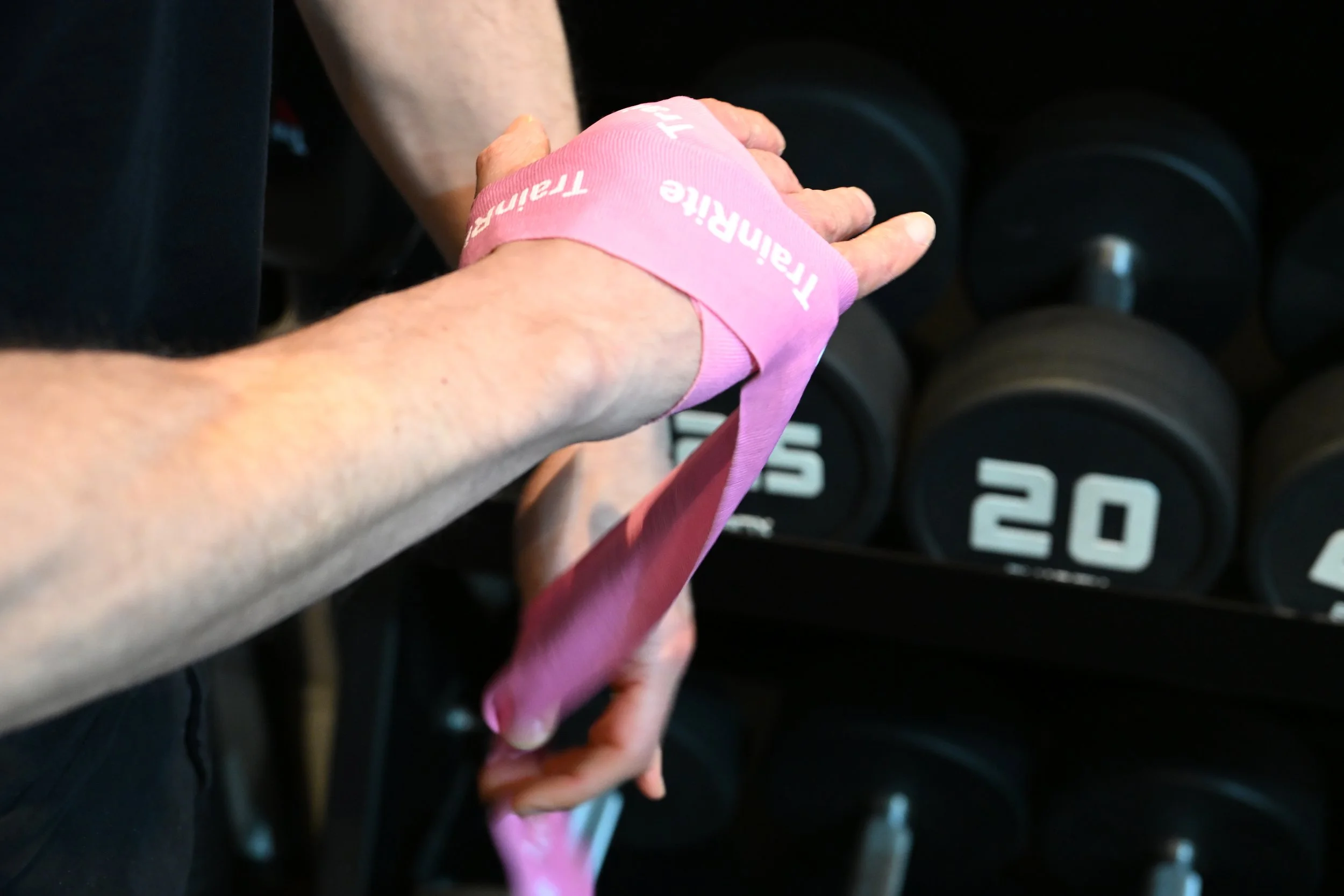 A person with a pink wrist strap wrapping their wrist in a gym setting, preparing for a boxing session.