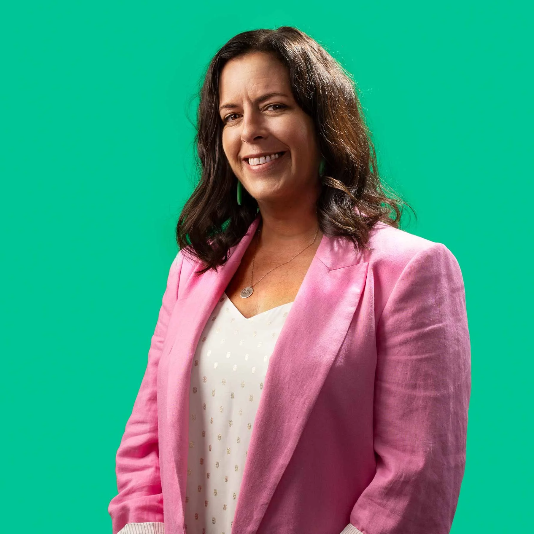 Smiling woman with shoulder length brown hair, wearing a bright pink suit and a white top patterned with gold polkadots