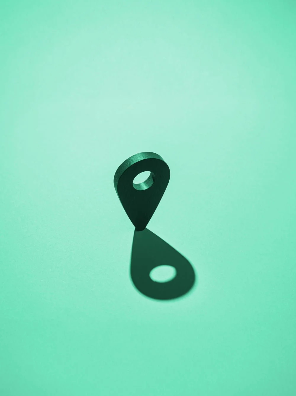 Location marker and it's dark shadow on a vibrant teal studio backdrop