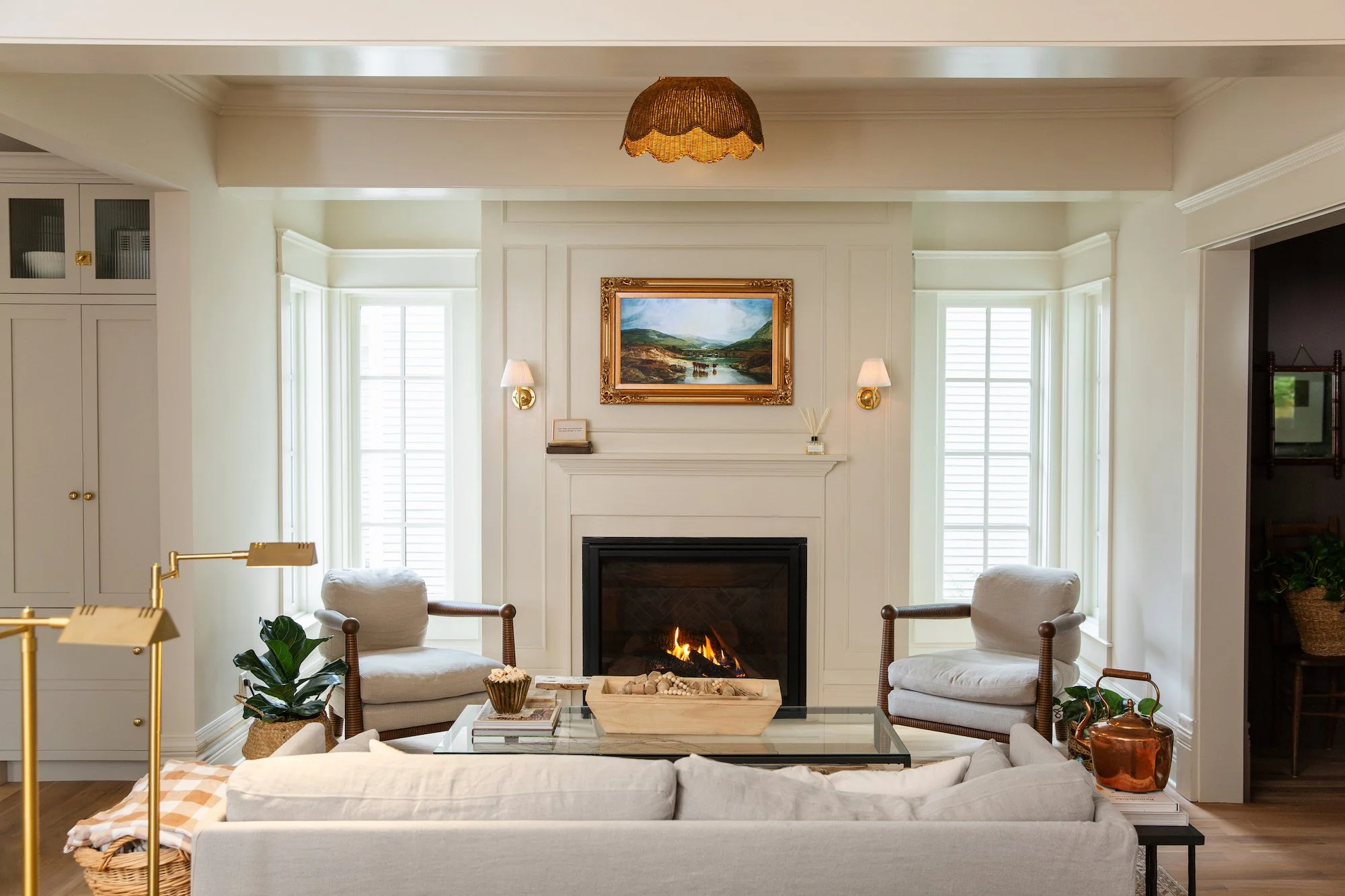 Living room with a fireplace, two armchairs, a glass coffee table, a white sofa, and a painting above the fireplace.