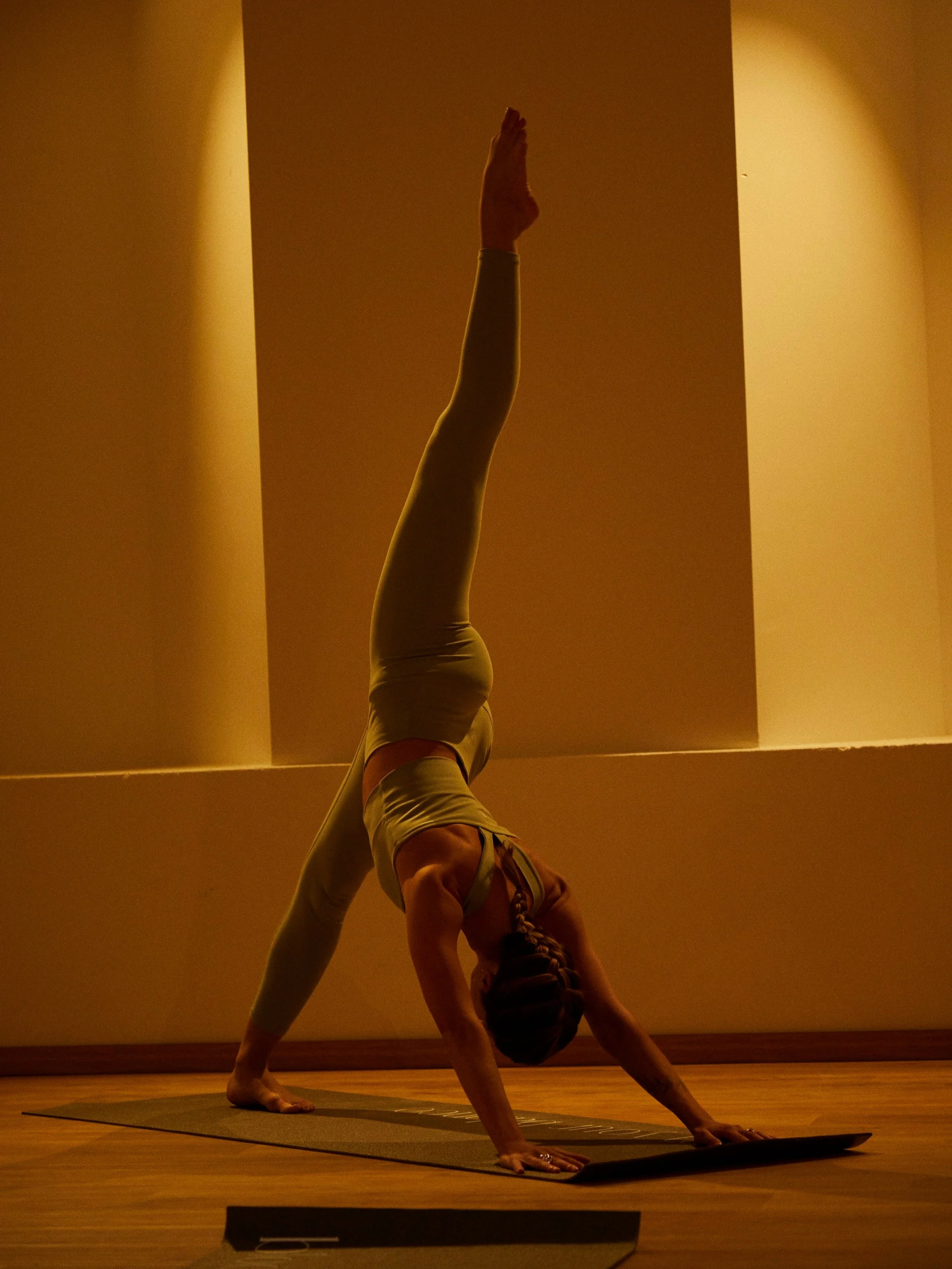 Donna che pratica GYROKINESIS® in una posizione a testa in giù con una gamba sollevata, in una stanza con luci calde.