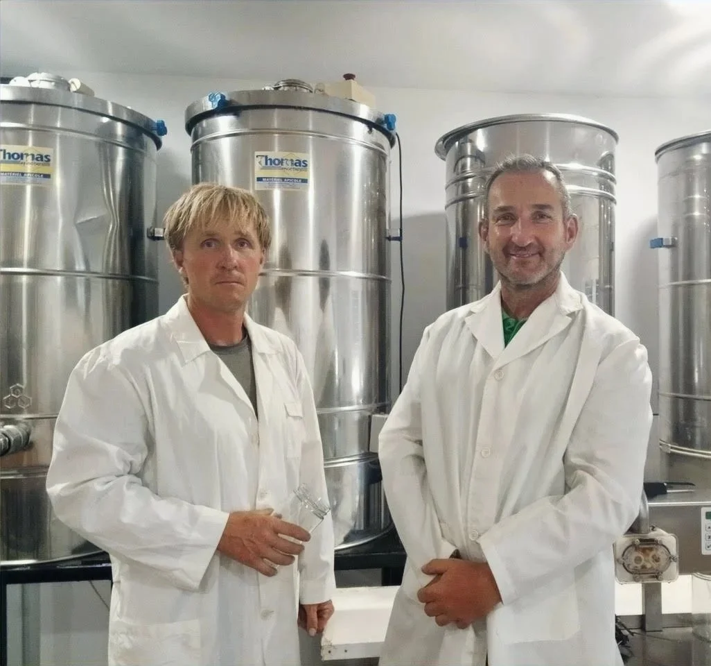 Two men in white lab coats standing in front of large stainless steel industrial fermenters or tanks in a laboratory or manufacturing facility.