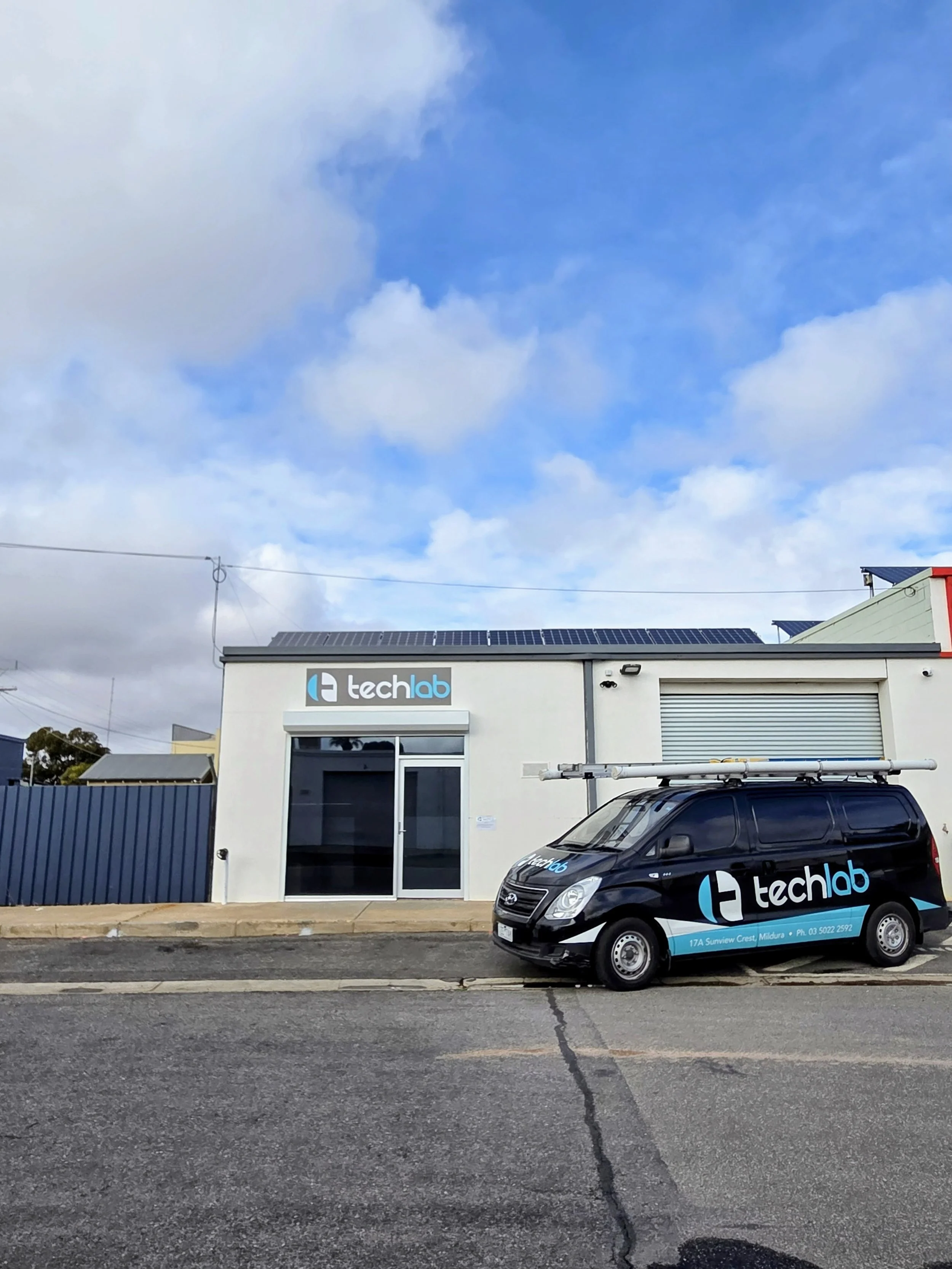 A small tech company storefront with a black company vehicle parked outside. The building has a sign that says 'techlab' and the vehicle has the same branding, including a logo and contact information.