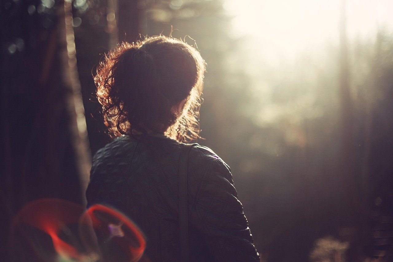 Person with curly hair standing outdoors in sunlight, facing away.