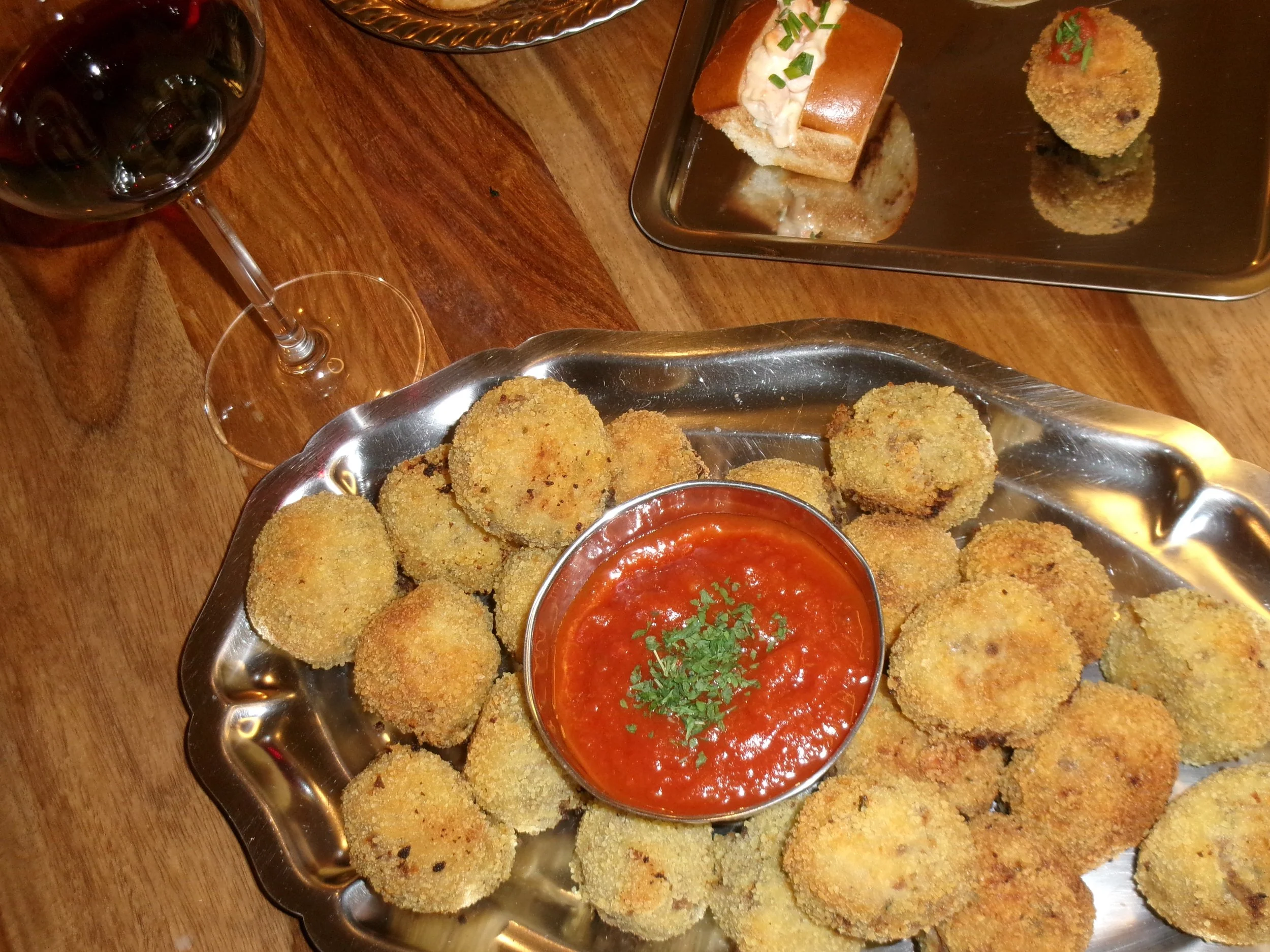 Assiette de croquettes frites au boeuf servies avec une sauce marinara garnie de persil, un verre de vin rouge et des amuse-bouches sur une table en bois, réalisé par Sofra Paris, traiteur événementiel à Paris.