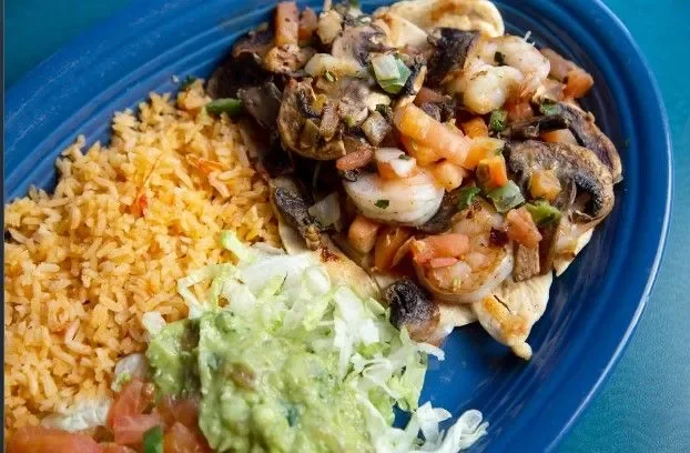 Plate with Mexican food including rice, shrimp with vegetables, and guacamole with lettuce and tomato.