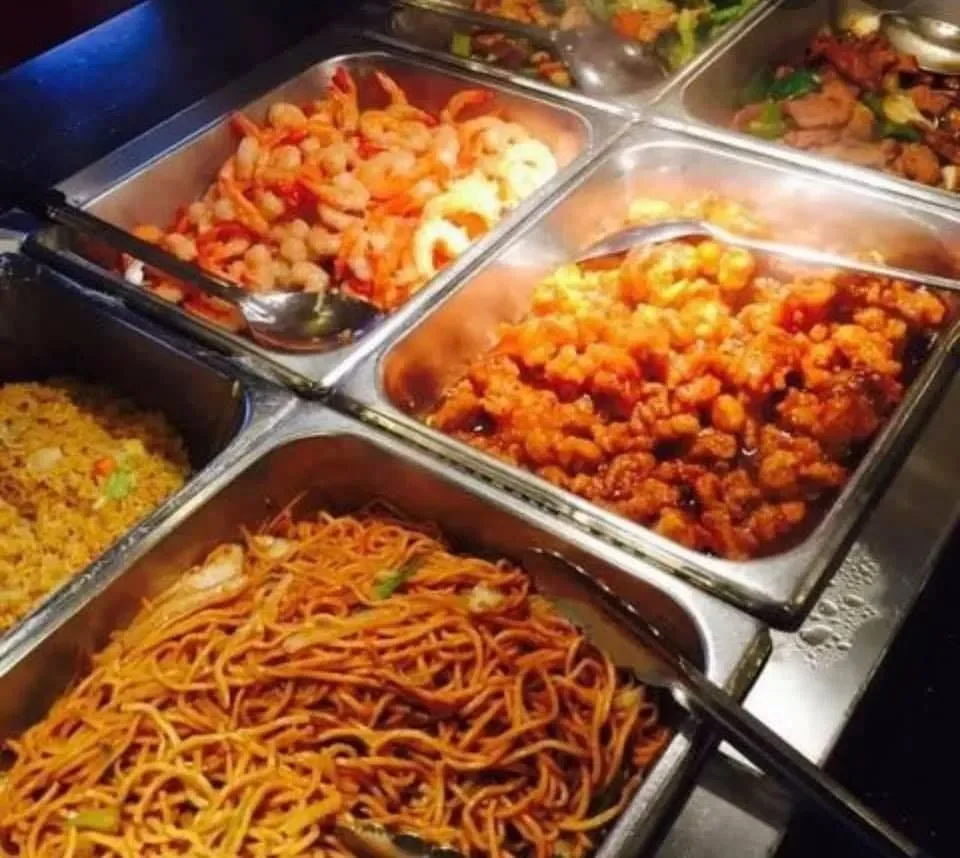 A buffet with trays of various Asian dishes, including fried rice, lo mein noodles, shrimp, and sweet and sour chicken.
