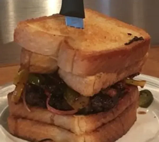 A large, stacked sandwich made with two slices of toasted bread with a thick filling of grilled meat, pickles, onions, and possibly other ingredients.