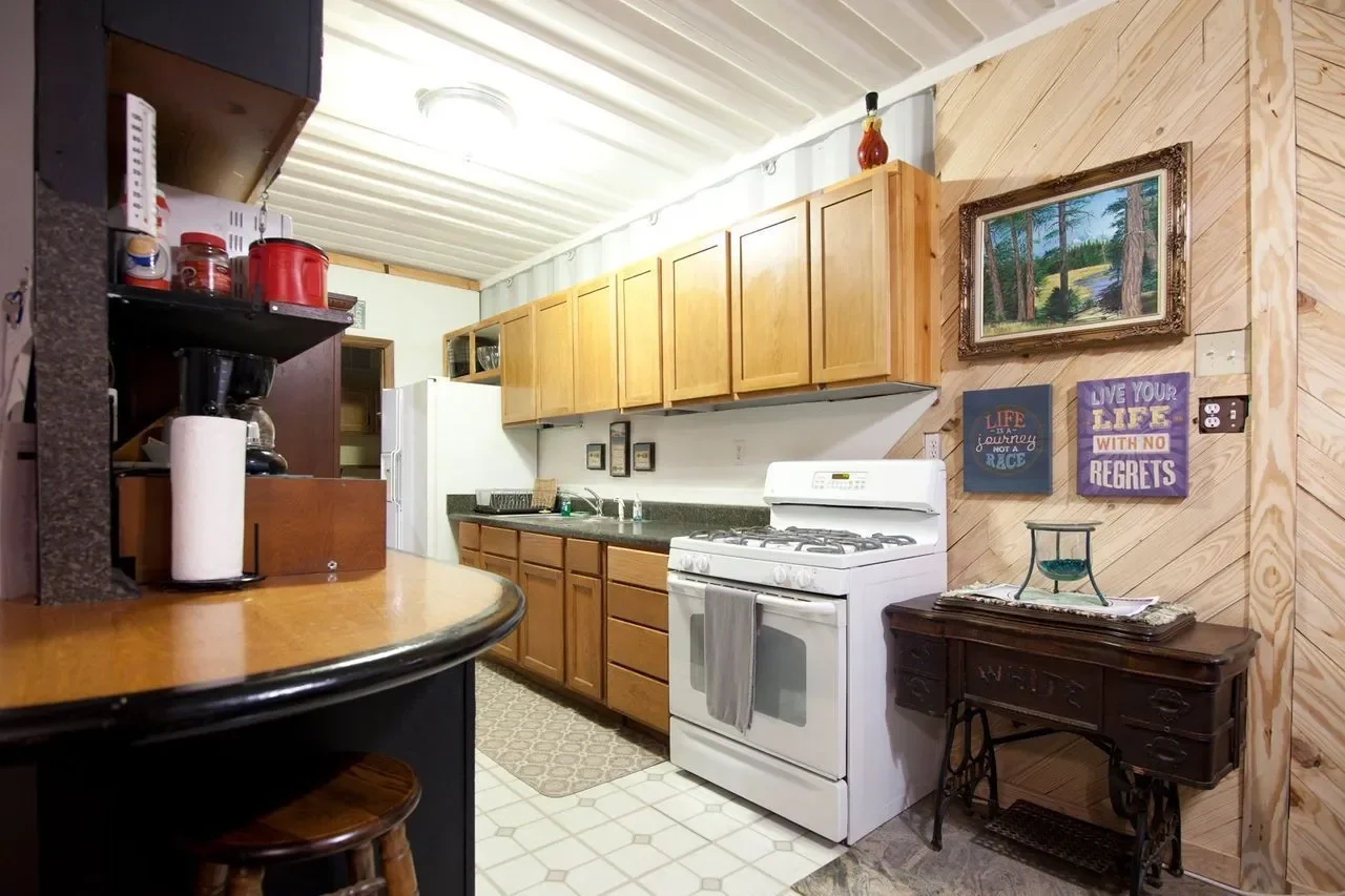 Kitchen with wooden cabinets, white stove, dark wooden table with decorative items, and framed artwork on wood-paneled wall.