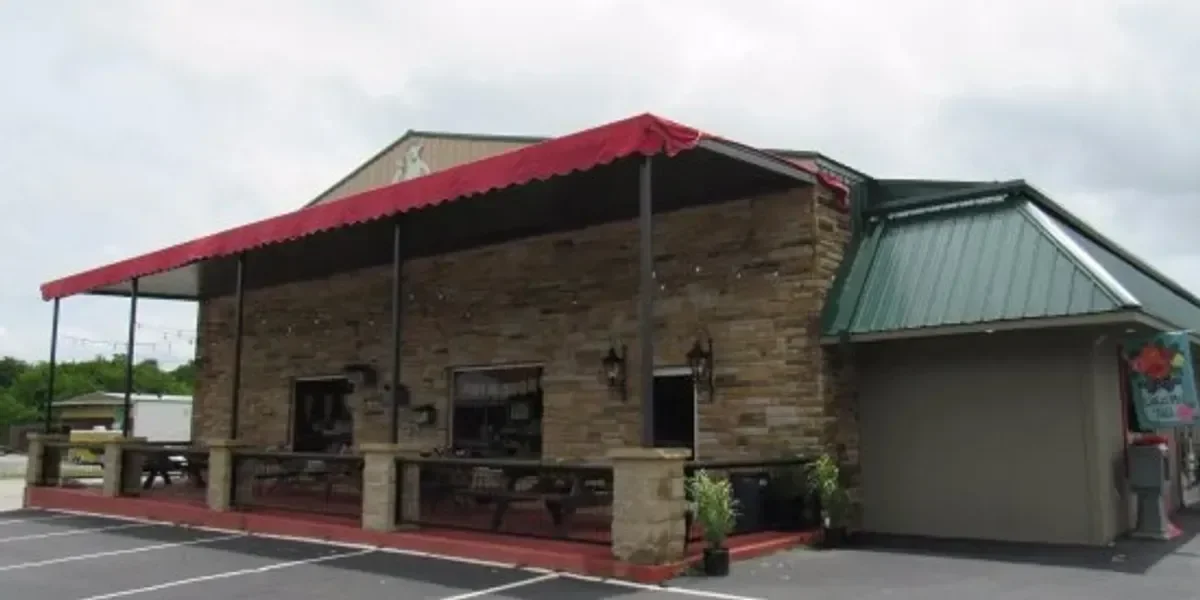A building with a stone facade, red awning, outdoor seating, and a vending machine in the parking lot.