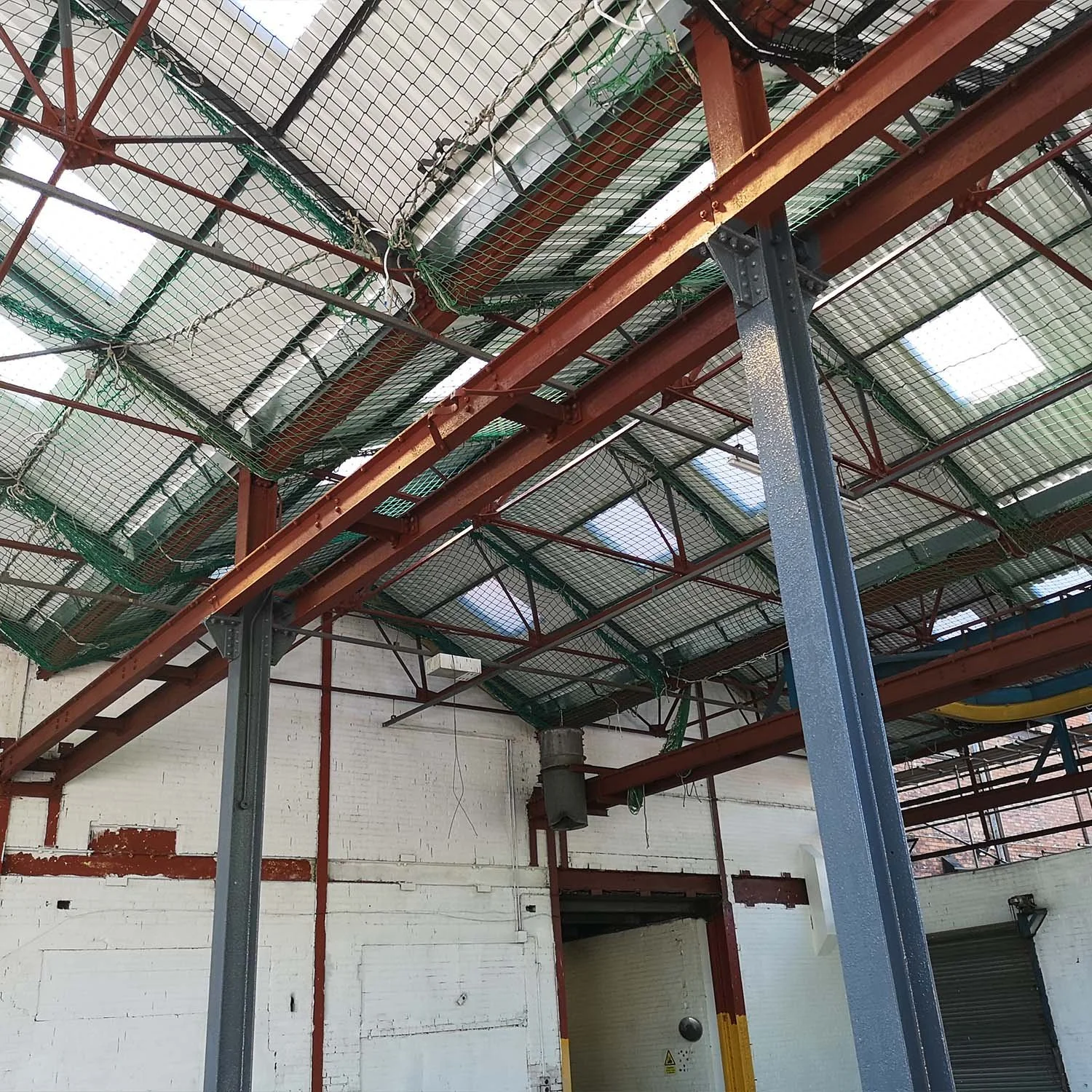 Construction site with steel beams and mesh ceiling under an industrial building interior.