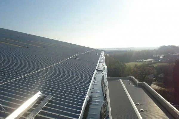 Close-up of a rooftop with solar panels and a skylight, with a scenic landscape in the background.