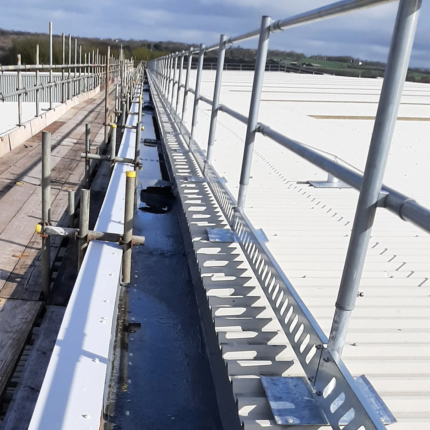 Construction scaffolding on a rooftop with cloudy sky and distant hills.