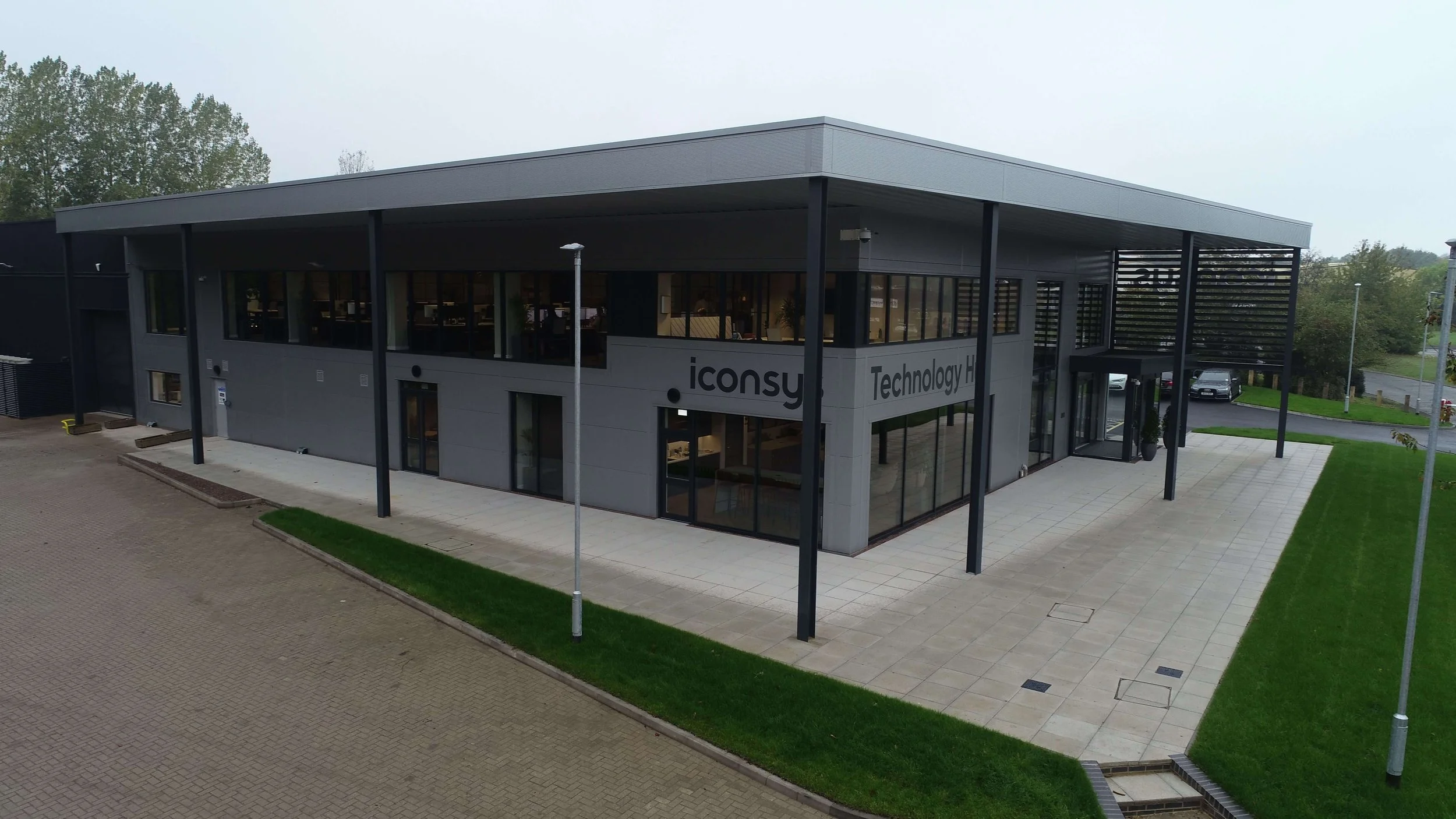 Modern two-story office building with glass windows, gray and black exterior, and signage reading 'iconsy' and 'Technology H'.