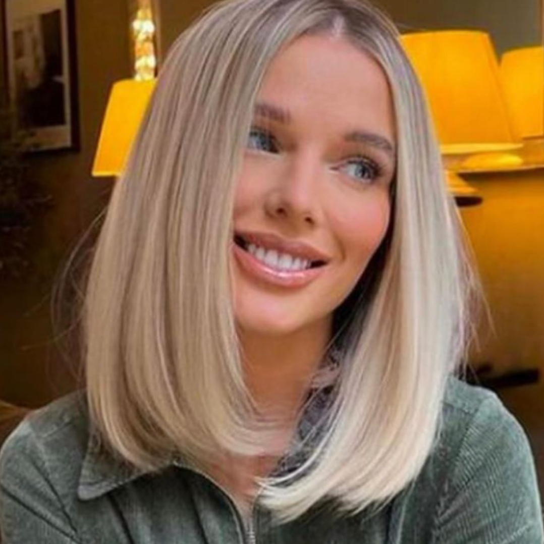 A woman with blonde hair smiling in a warmly lit room with yellow lamps in the background.