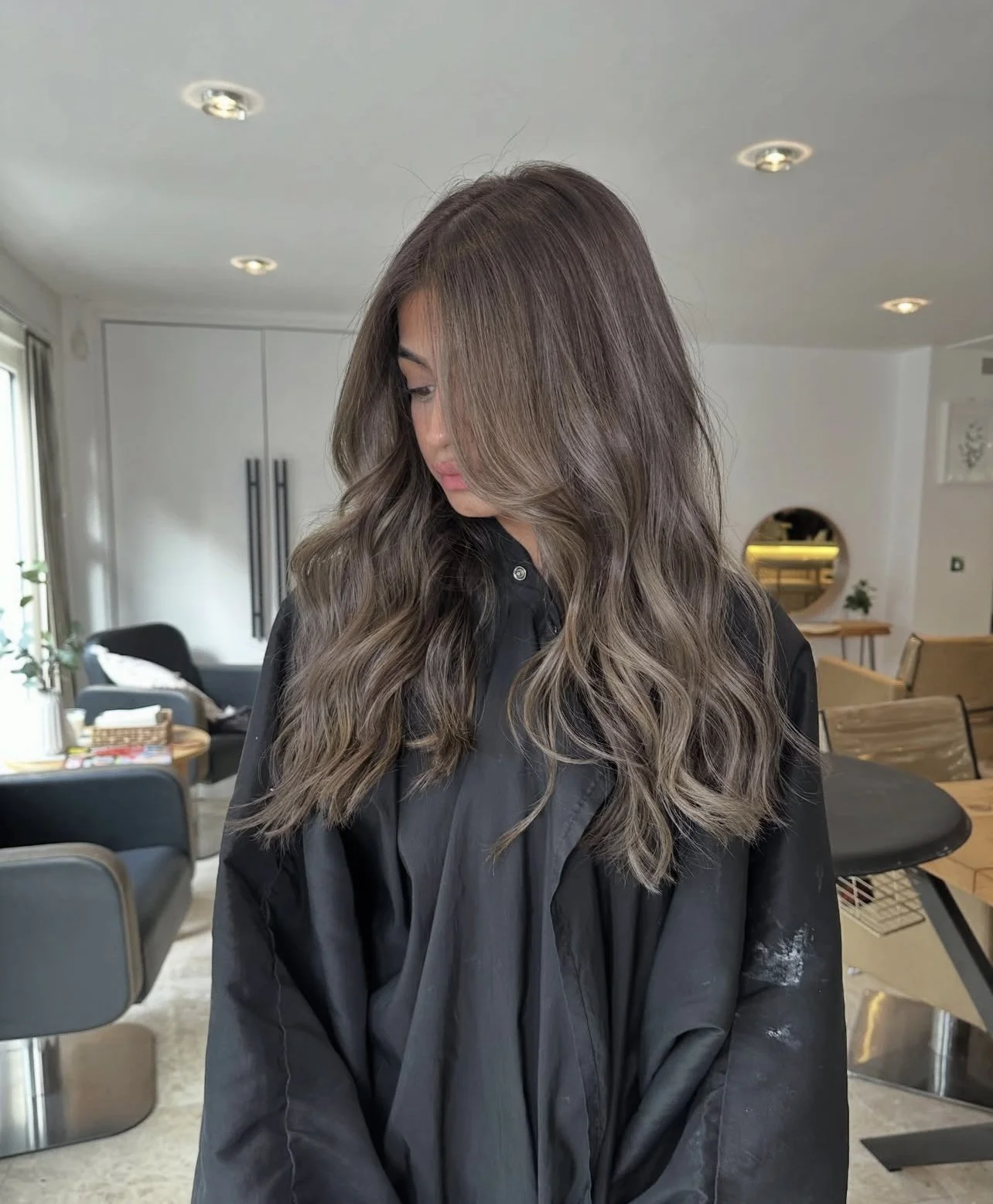 Woman with long wavy brown hair looking down inside a modern, bright home.