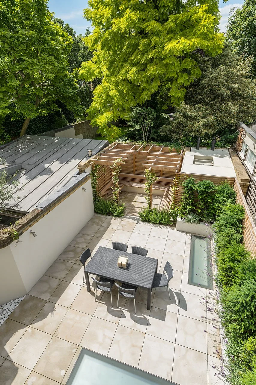 Aerial view of a modern backyard patio with a dining table, six chairs, a garden area, trees, and a wooden privacy fence.