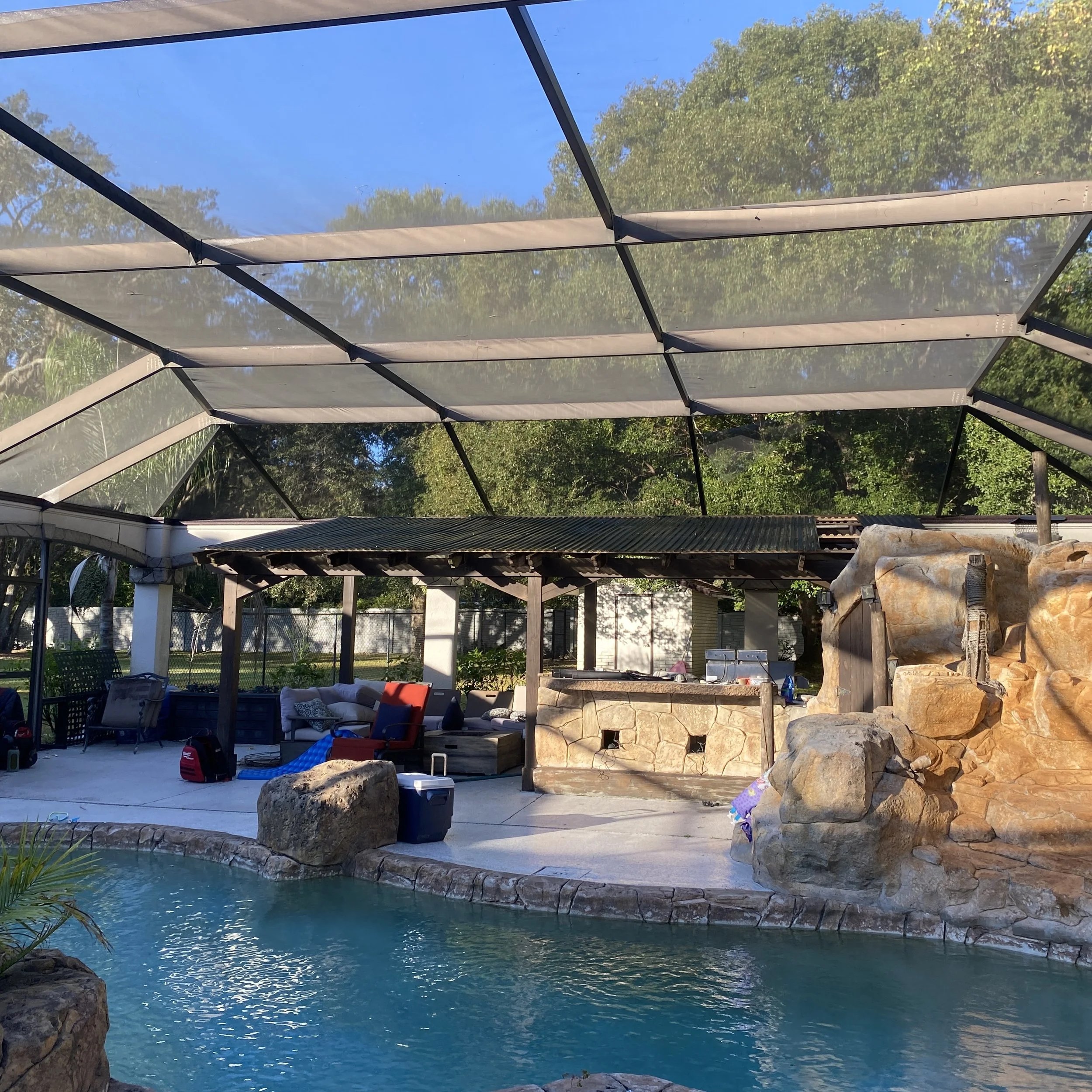 Backyard with swimming pool, outdoor seating area, and screened enclosure with trees in the background.