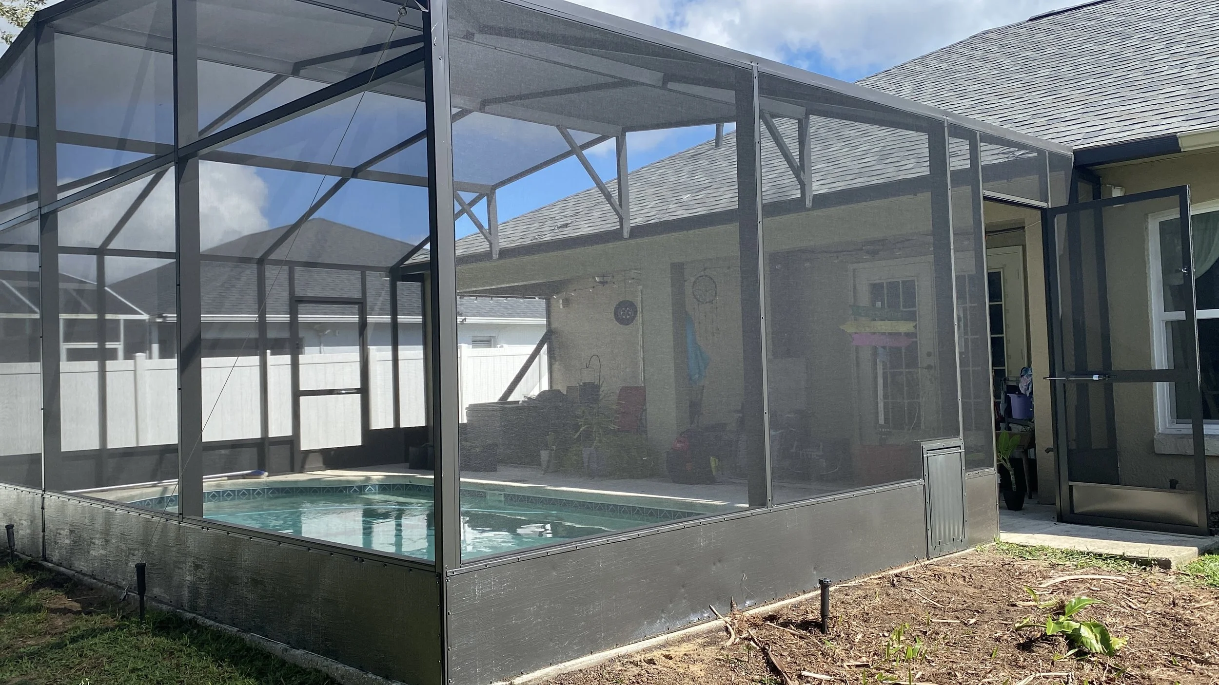 A backyard enclosed swimming pool with a screened enclosure on a sunny day.