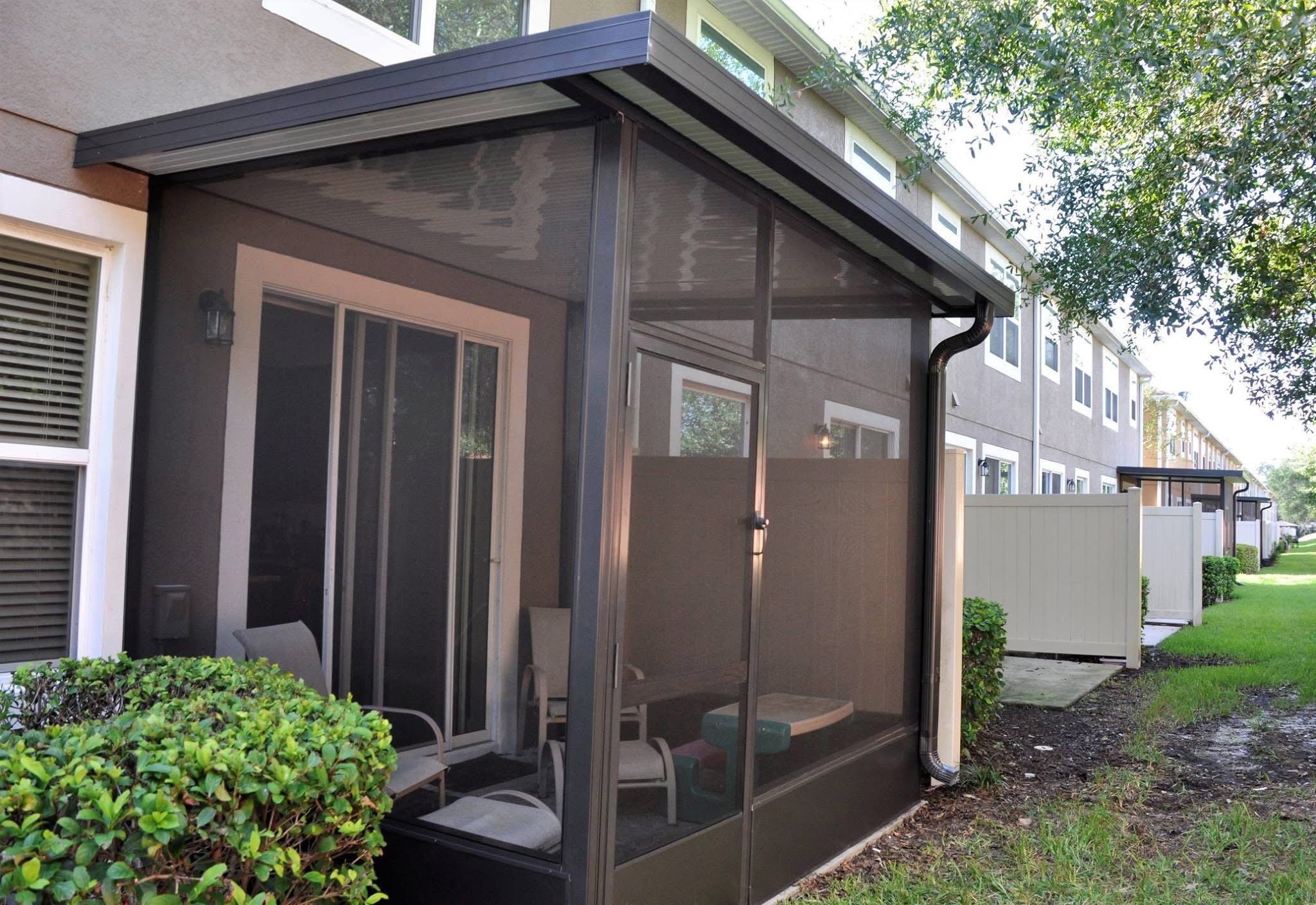 Back patio enclosed with black screened panels, attached to a multi-story apartment building, with patio furniture inside and a white fence nearby.