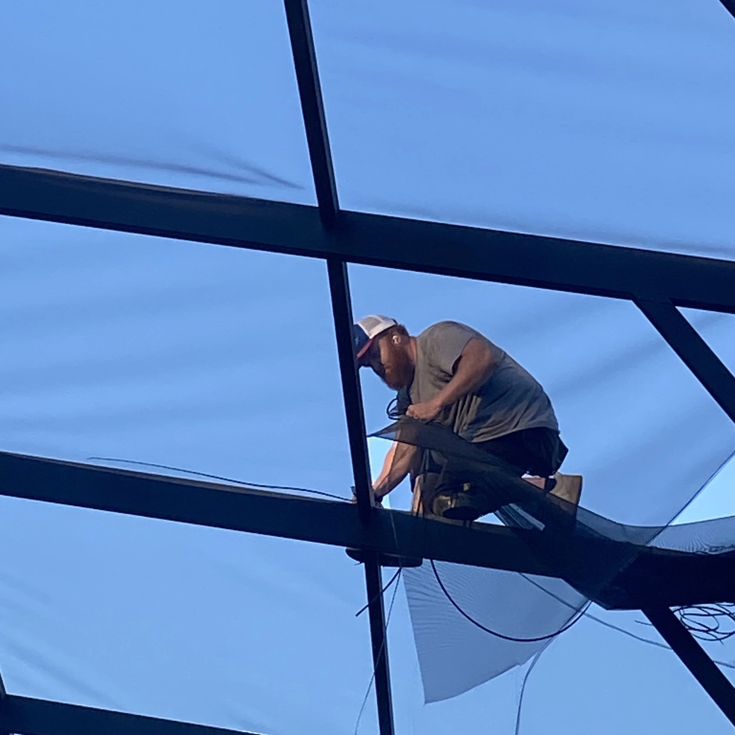 A worker on a construction lift working on roof panels against a blue sky.